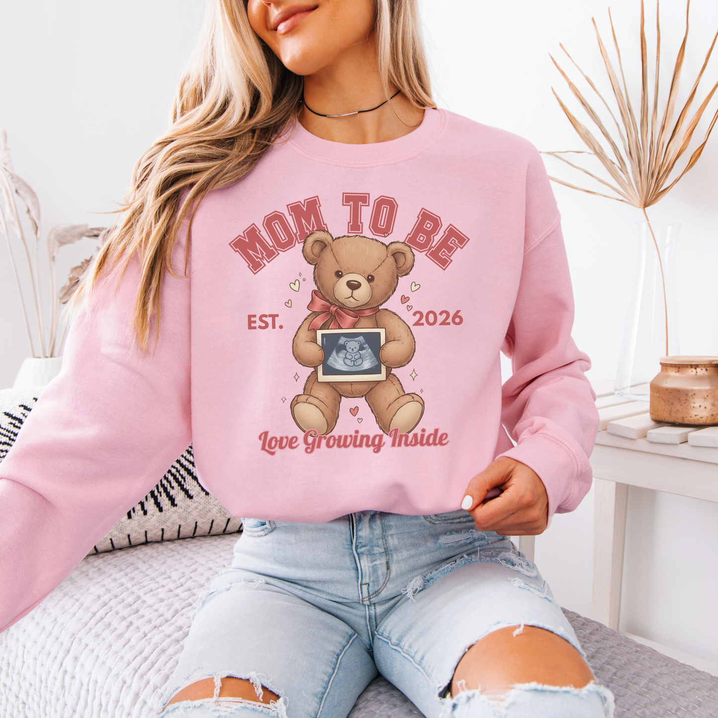 Person wearing a pink 'Mom to Be' sweatshirt with a teddy bear graphic.