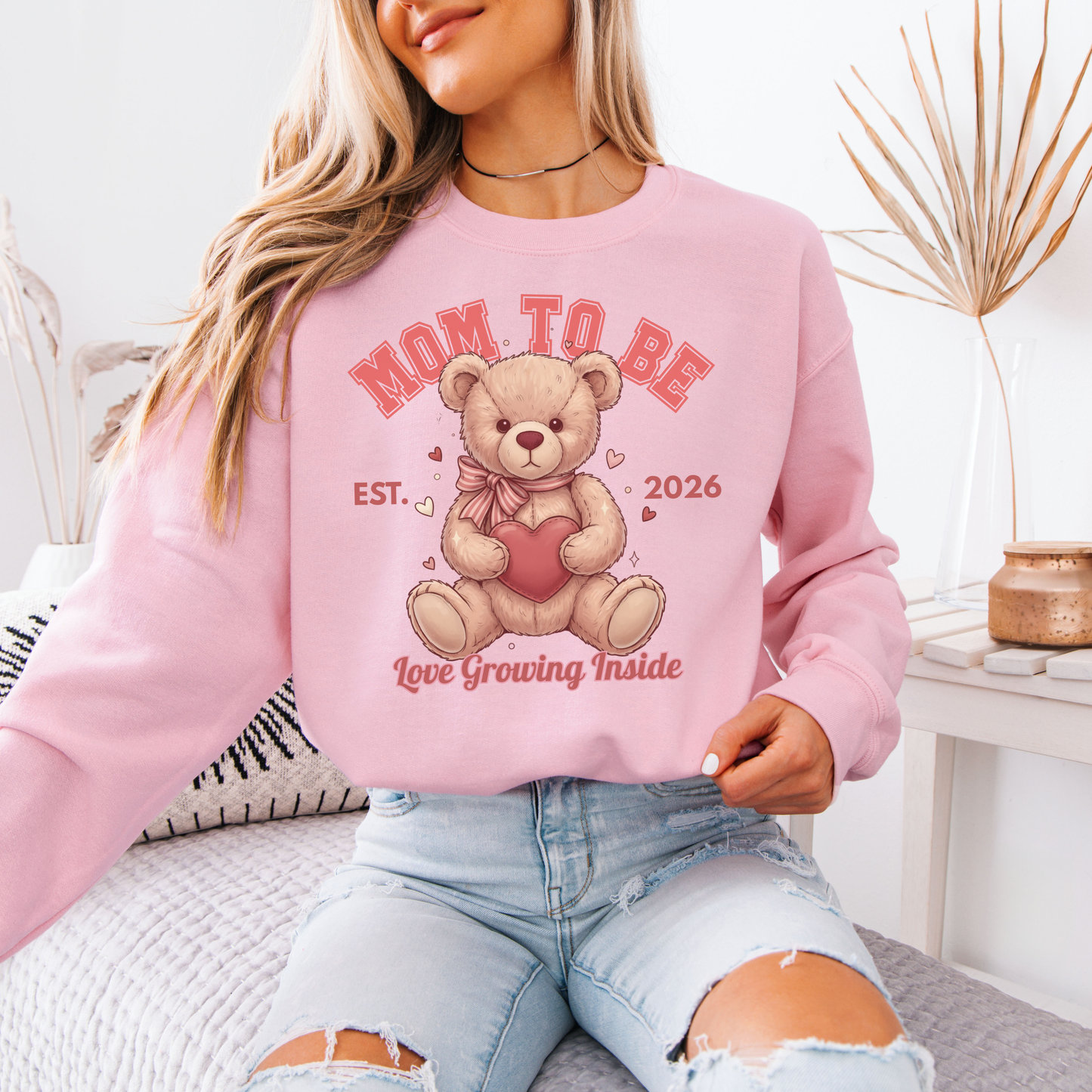 Person wearing a pink 'Mom to Be' sweatshirt with a teddy bear graphic.