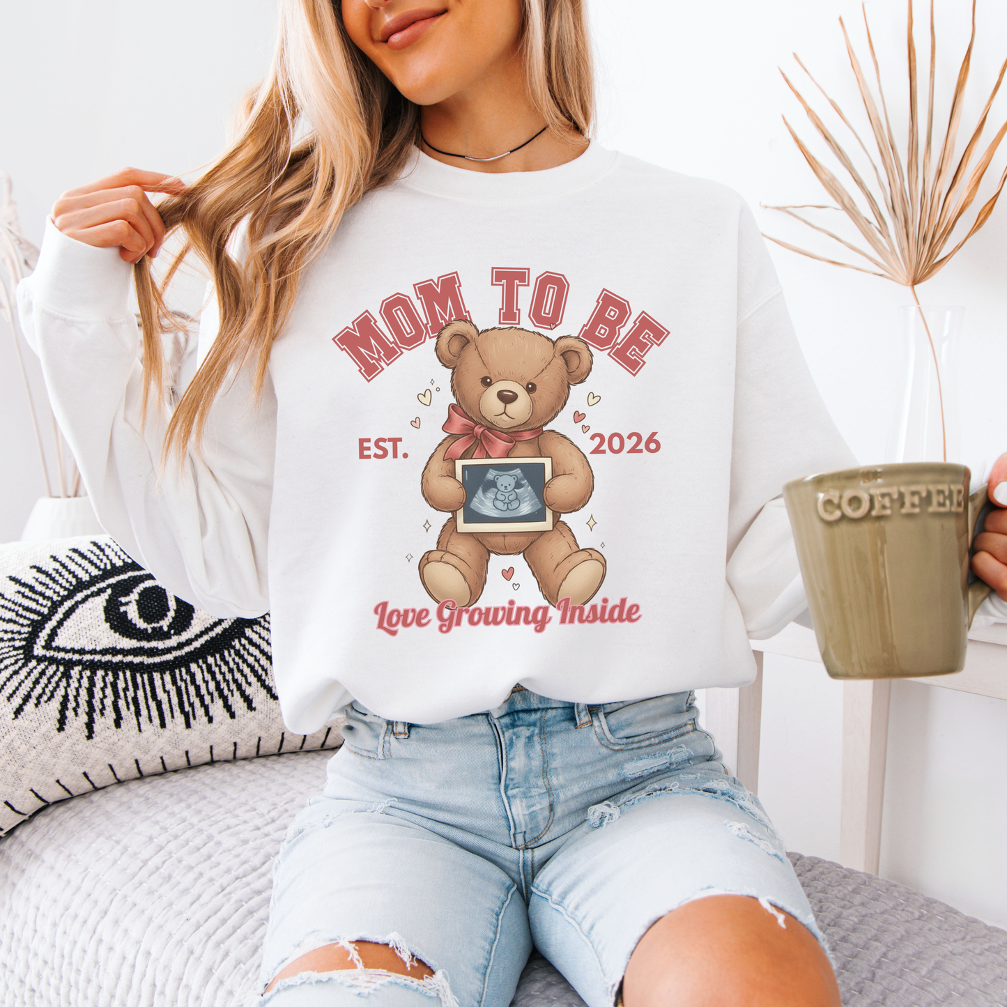 Woman wearing a 'Mom to Be' sweatshirt with a teddy bear graphic