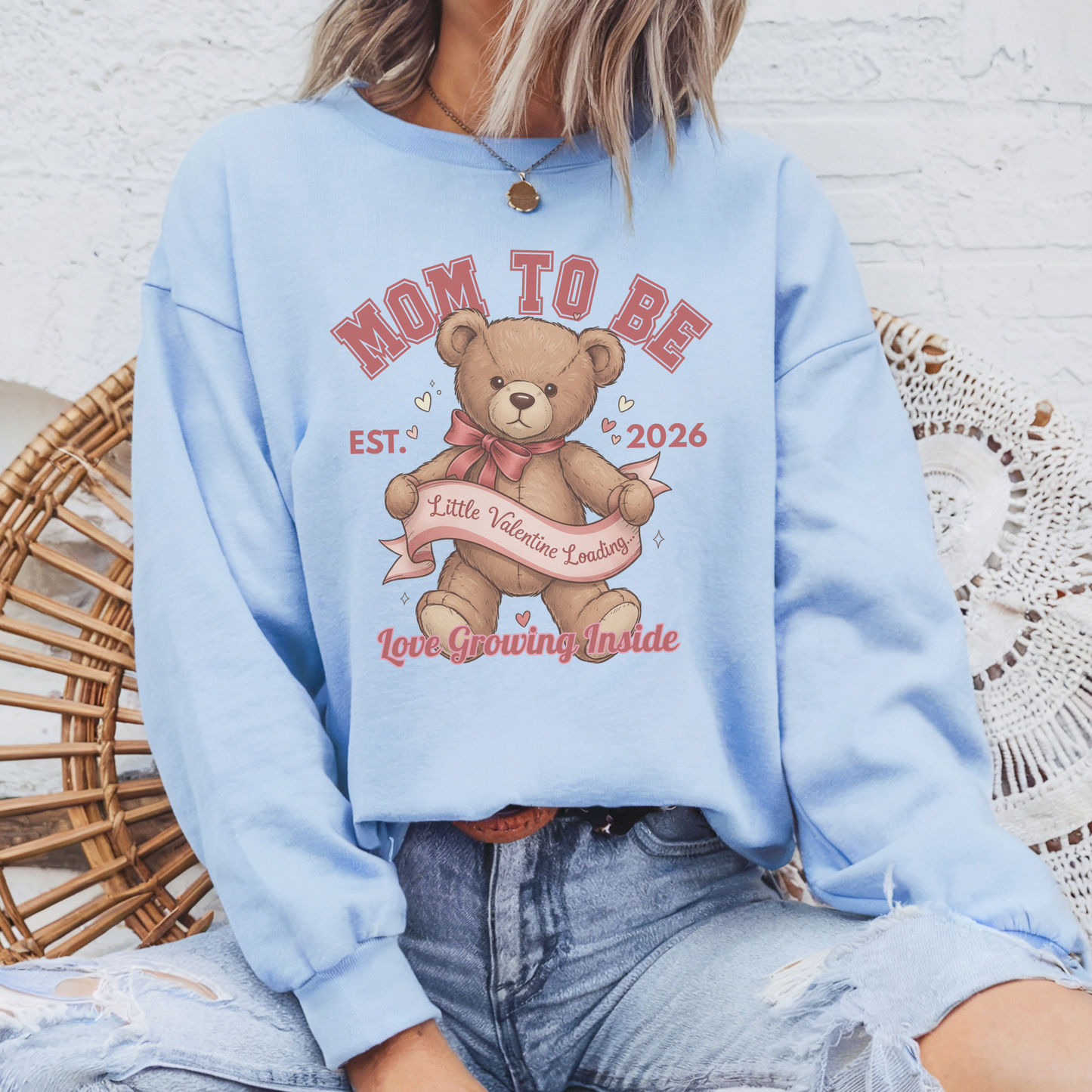 Light blue sweatshirt with teddy bear graphic and text, worn by a person sitting on a wicker chair.