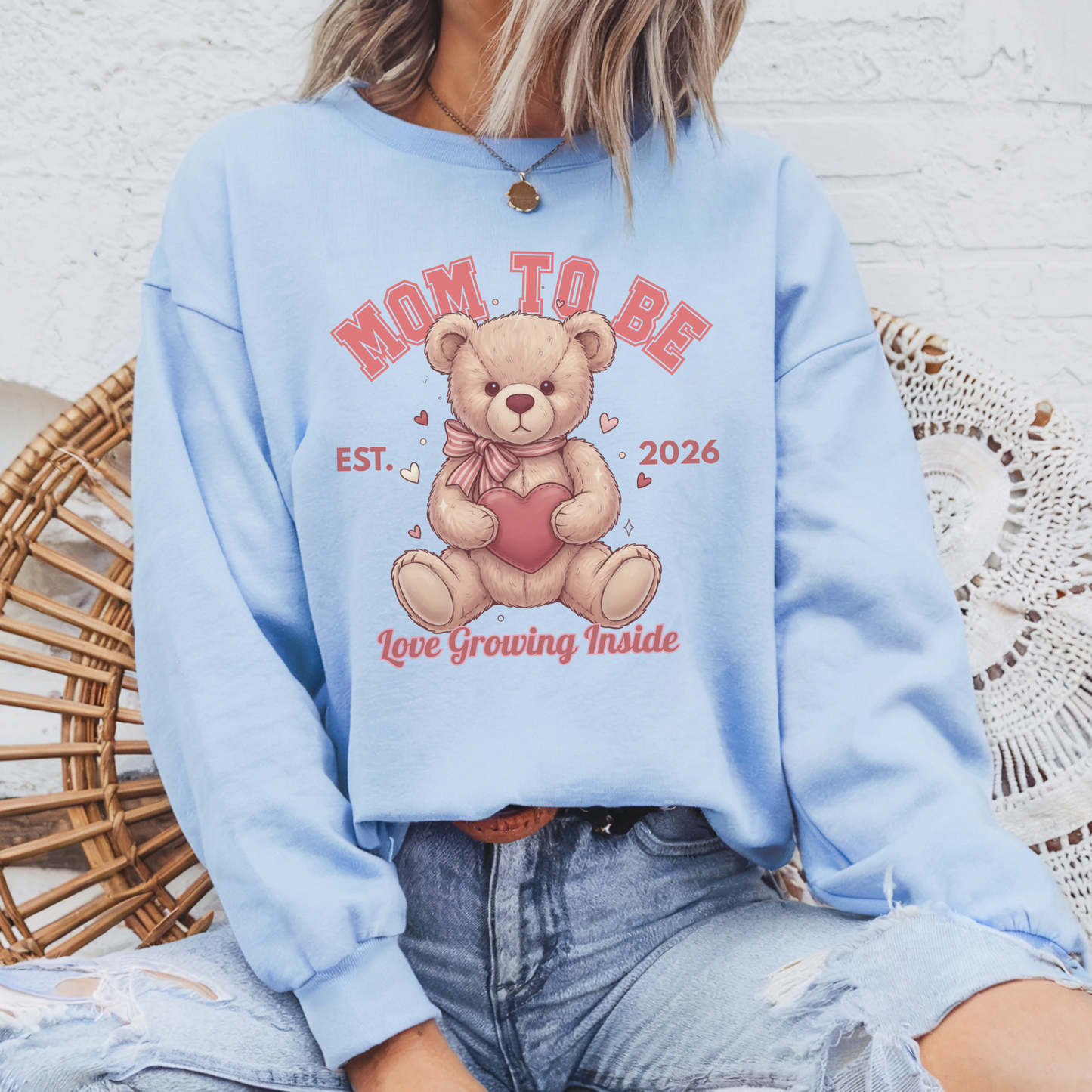 Light blue sweatshirt with teddy bear graphic and text, worn by a person sitting on a woven chair.