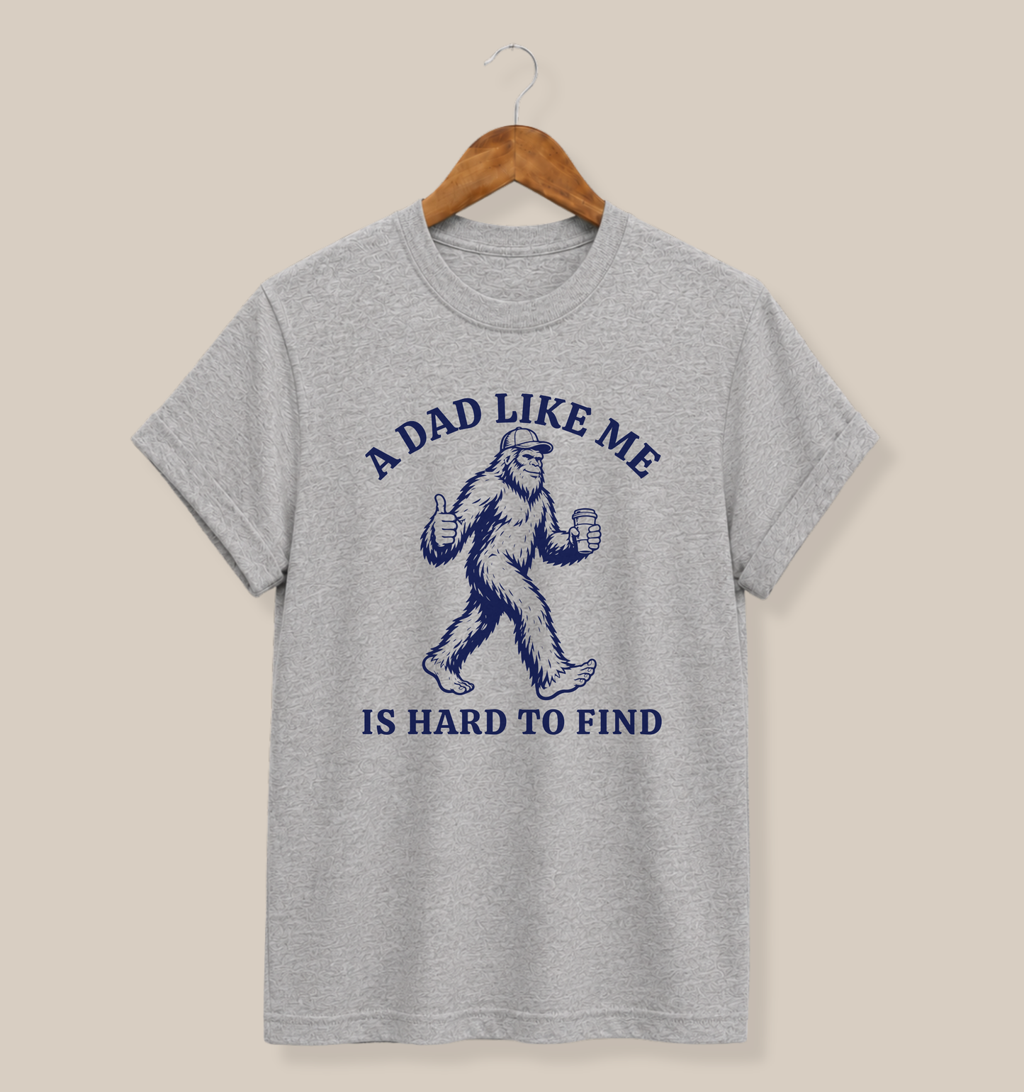 Bella + Canvas 3001 t-shirt in athletic heather grey featuring a funny dad design with a Bigfoot holding a coffee cup and thumbs up alongside the phrase “A Dad Like Me Is Hard To Find” in navy blue lettering.