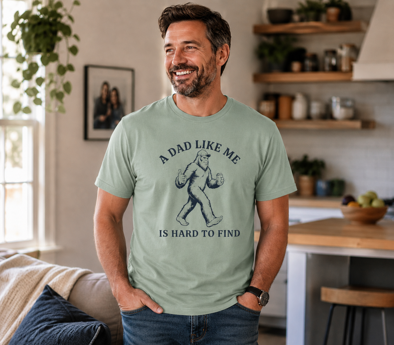 Man wearing a Comfort Colors 1717 t-shirt in bay green featuring a funny Bigfoot dad design with the phrase “A Dad Like Me Is Hard To Find” in dark navy lettering while standing in a cozy home setting.