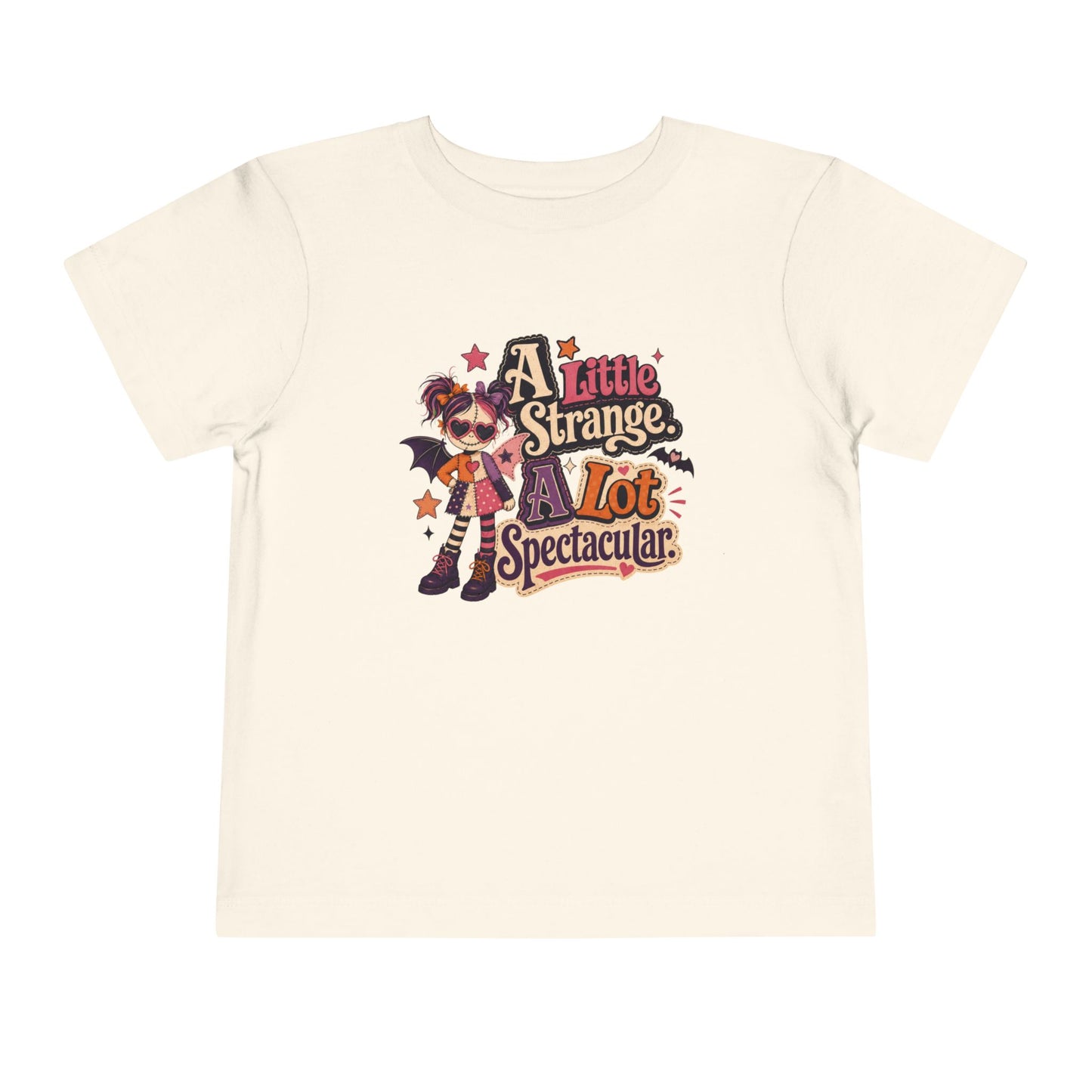 Natural toddler T-shirt featuring a colorful spooky doll with bat wings and the phrase “A Little Strange, A Lot Spectacular.”