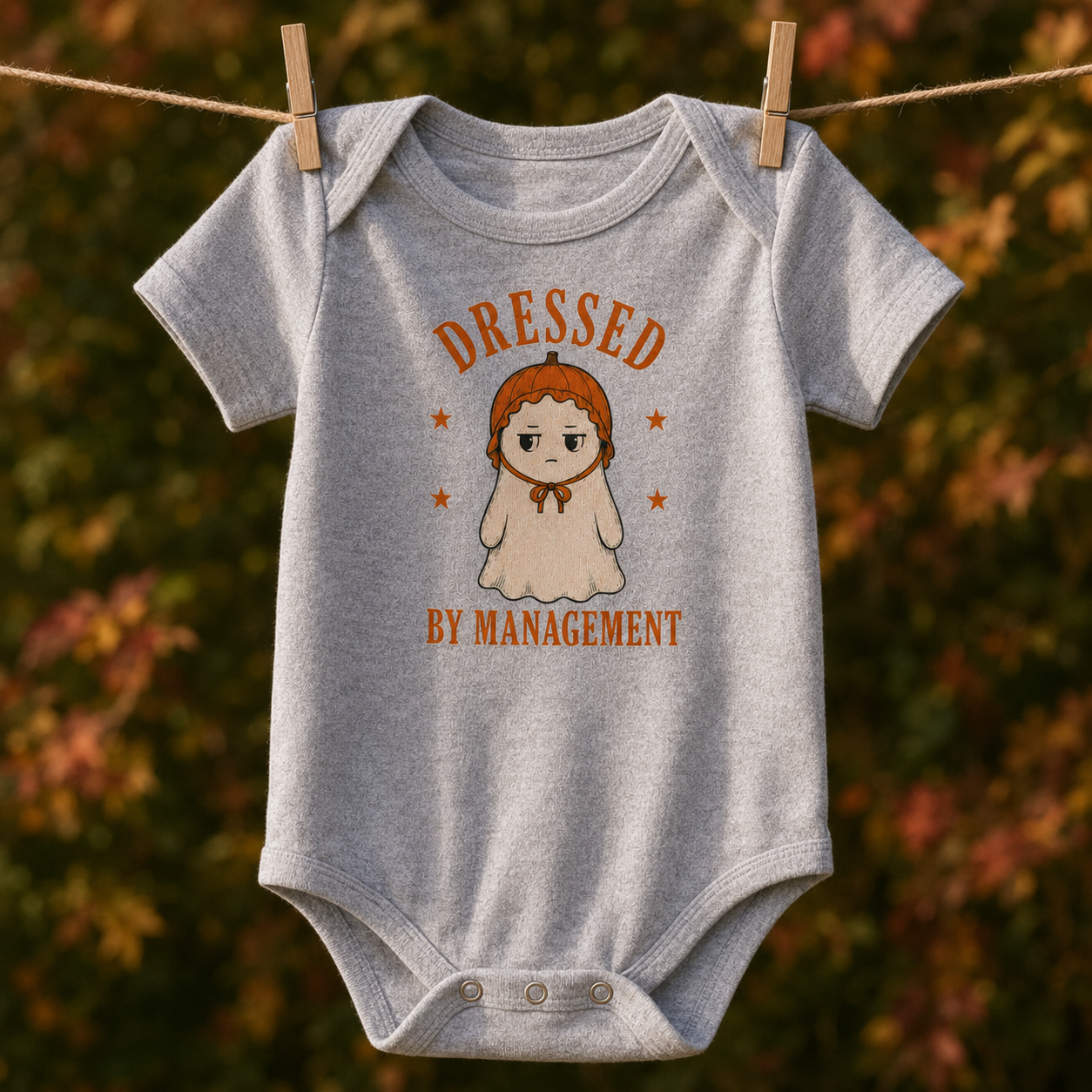 Bella + Canvas 100B infant one piece in Heather Grey featuring a cute ghost wearing a pumpkin bonnet with the phrase "Dressed by Management." Cozy Halloween baby bodysuit perfect for newborns, infants, baby's first Halloween, pumpkin patch outings, fall photos, and spooky season celebrations.