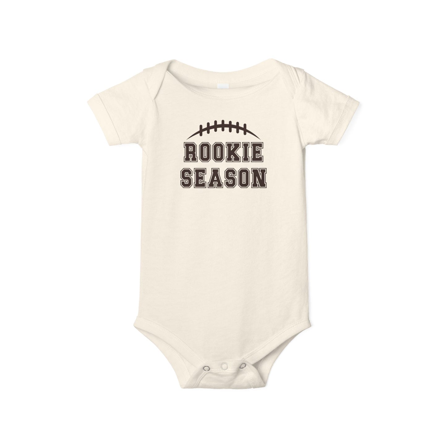 Bella + Canvas 100B natural infant bodysuit featuring a brown football graphic and "Rookie Season" text. Soft baby football outfit perfect for football season, game days, newborn photos, baby showers, and future football fans.