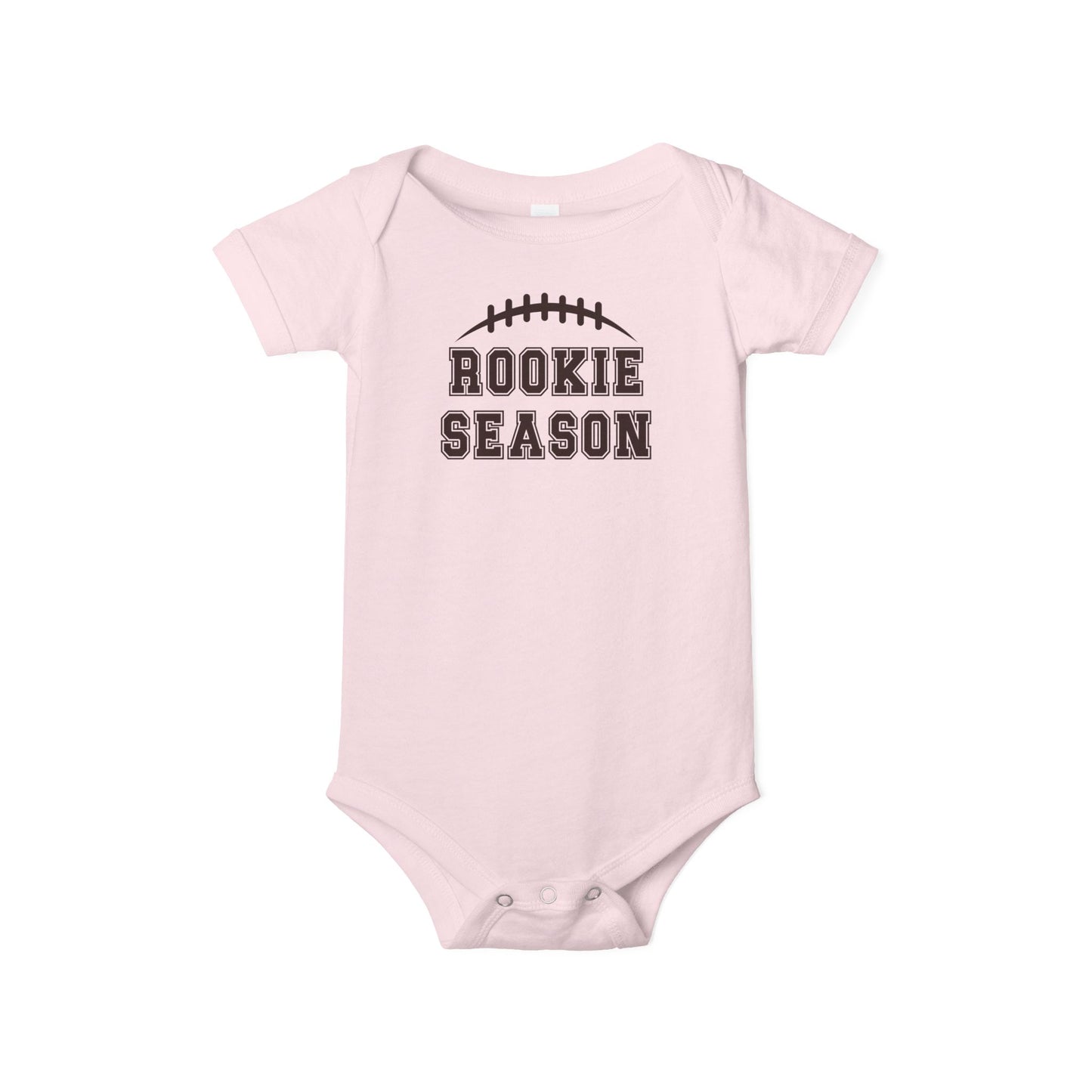 Bella + Canvas 100B pink infant bodysuit featuring a brown football graphic and "Rookie Season" text. Cute football baby outfit perfect for game days, football season, baby showers, newborn photos, and little football fans.