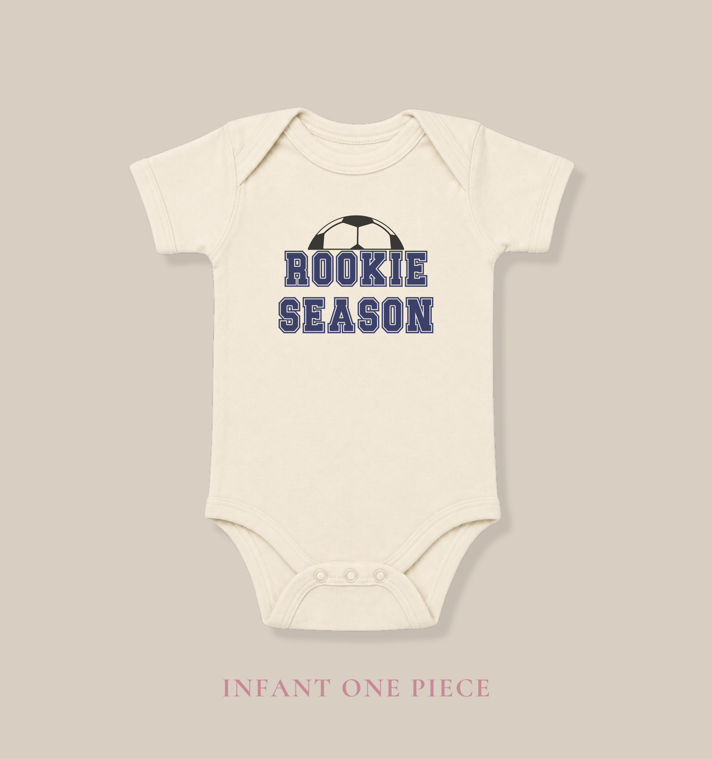 Bella + Canvas 100B baby bodysuit in natural featuring the phrase “Rookie Season” in navy varsity lettering with a soccer ball graphic. Cute soccer baby one-piece for infant boys and girls, perfect for first soccer season, game day outfits, soccer family photos, baby shower gifts, and newborn sports fans.