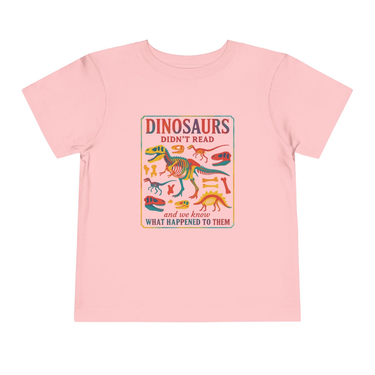 Bella + Canvas 3001T toddler t-shirt in pink featuring a colorful dinosaur skeleton graphic and the funny quote “Dinosaurs Didn’t Read and We Know What Happened to Them.” Cute dinosaur shirt for toddlers who love books, reading, dinosaurs, preschool, and back-to-school adventures.