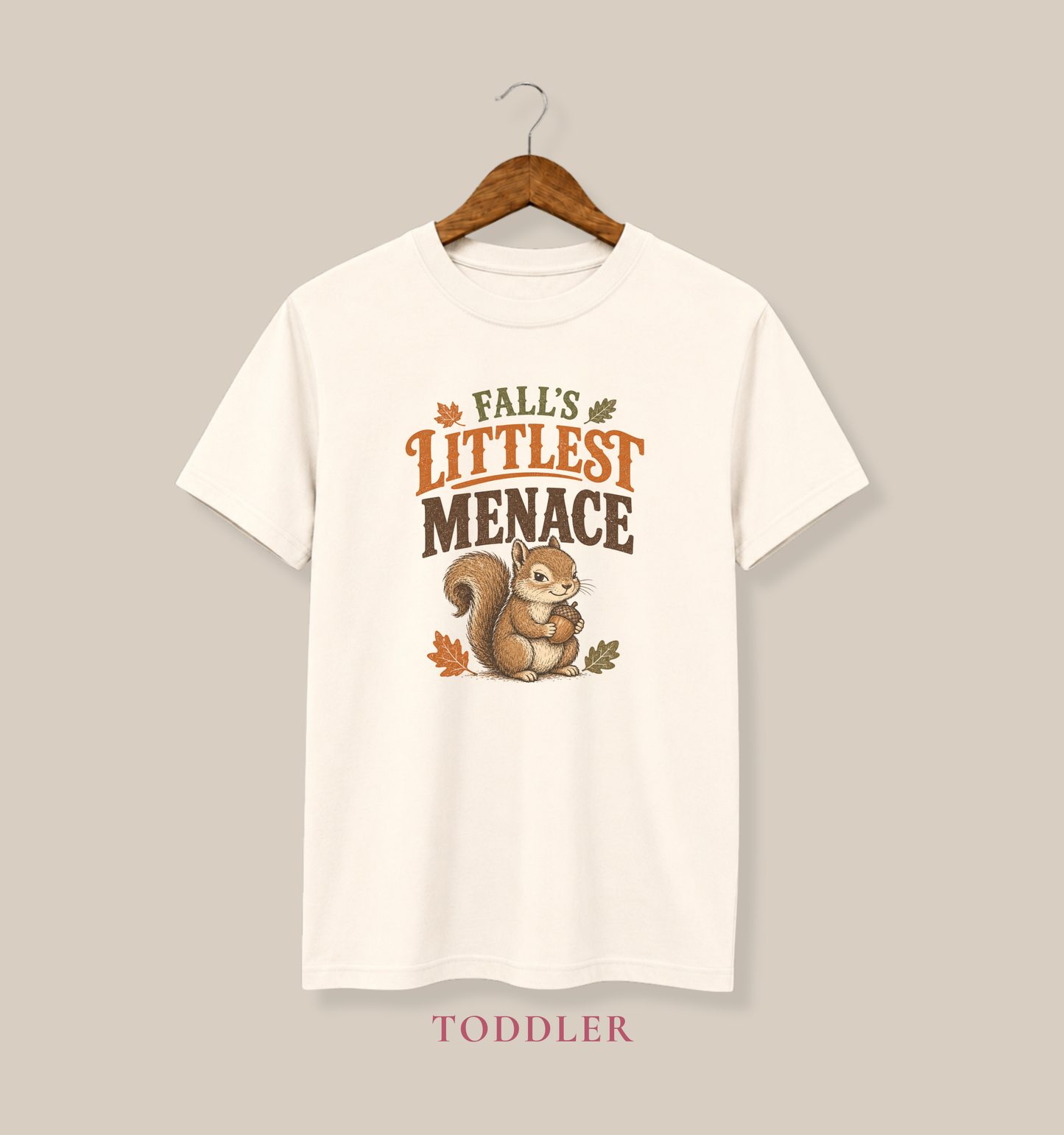 Natural Bella + Canvas 3001T toddler t-shirt featuring a mischievous squirrel holding an acorn with the phrase "Fall's Littlest Menace." Cute autumn toddler shirt perfect for pumpkin patches, fall festivals, Halloween, family photos, and everyday seasonal wear.
