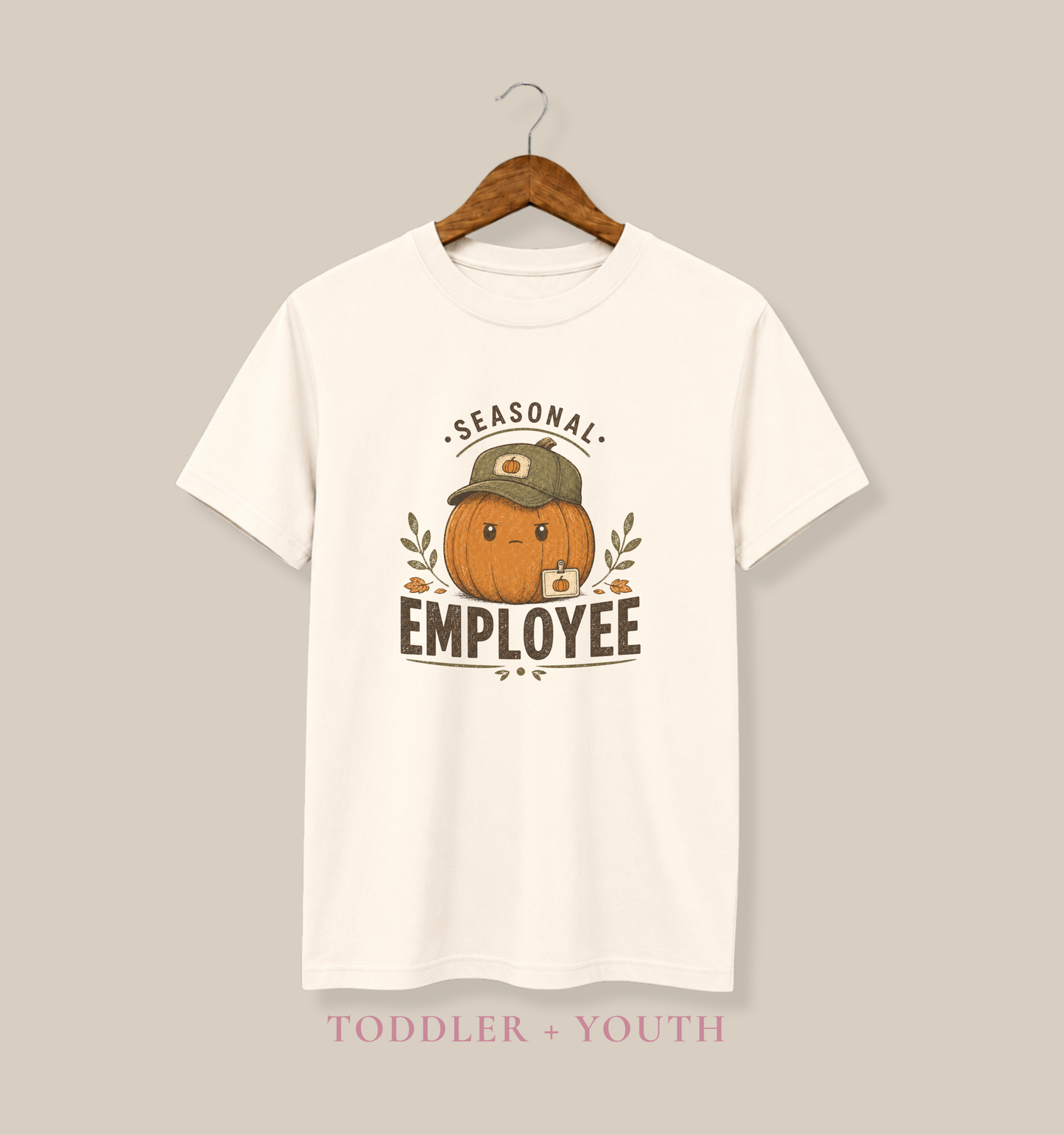 Natural Bella + Canvas 3001Y youth t-shirt featuring a grumpy pumpkin wearing a baseball cap with the phrase "Seasonal Employee." Cute fall graphic tee for kids, perfect for pumpkin patch visits, autumn festivals, Halloween, school, and seasonal family photos.
