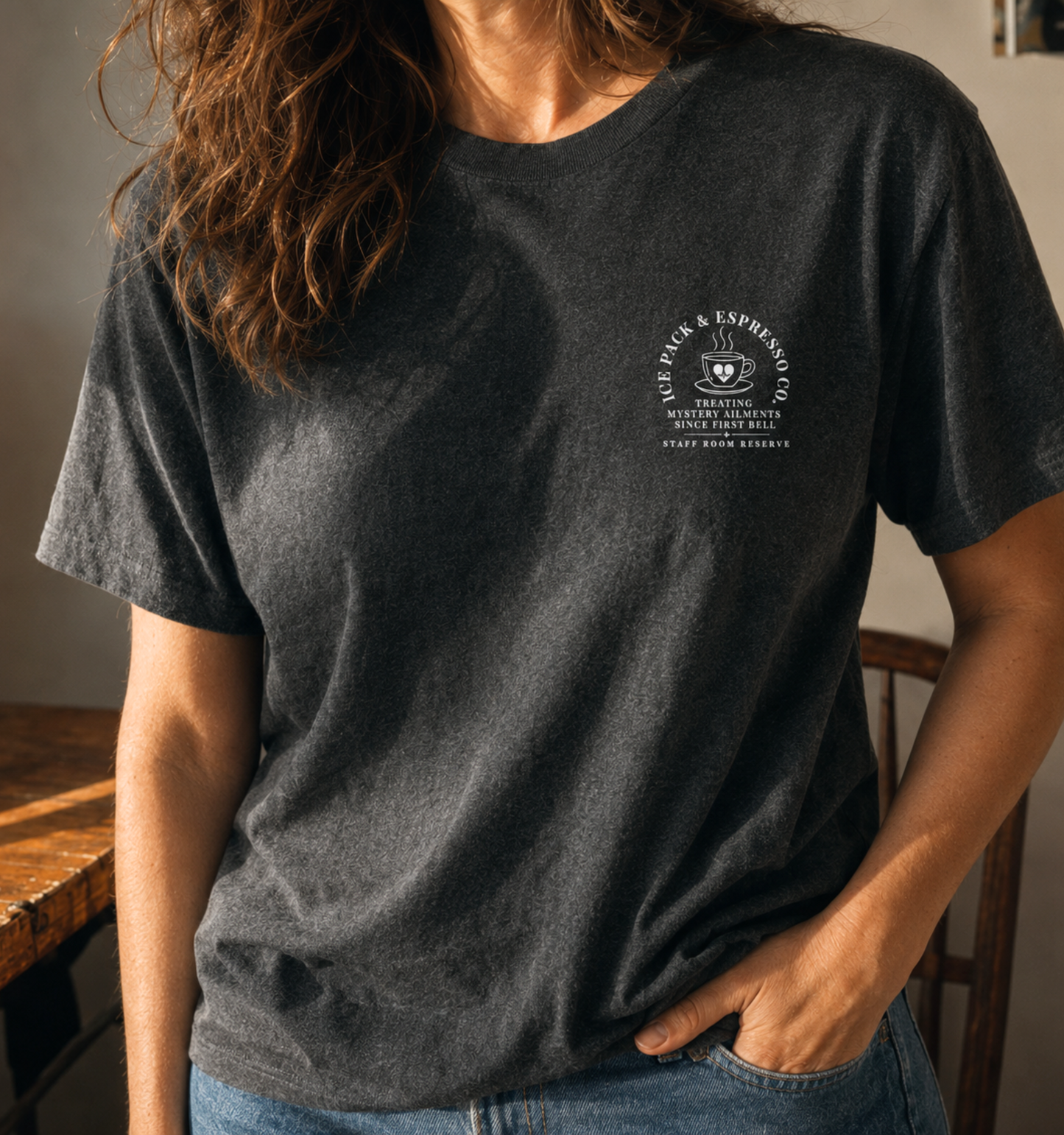 Bella + Canvas 3001 unisex t-shirt in Dark Grey Heather featuring a small left chest "Nurse Pack & Espresso Co." coffee-themed graphic with the phrases "Treating Mystery Ailments Since First Bell" and "Staff Room Reserve." A cozy nurse-inspired graphic tee perfect for school nurses, healthcare professionals, and everyday casual wear.