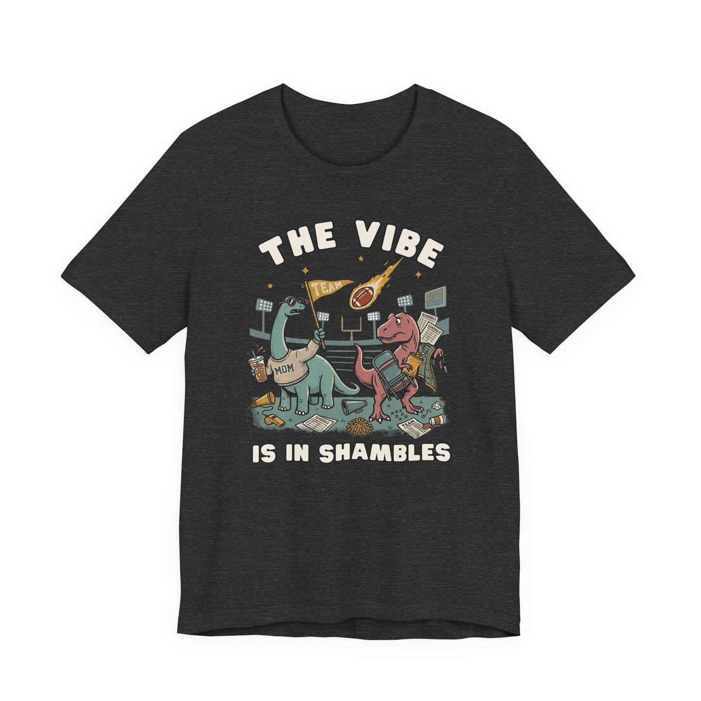 Bella + Canvas 3001 dark heather athletic grey t-shirt featuring two overwhelmed dinosaurs at a football stadium surrounded by a folding chair, coffee, snacks, team flag, and game day gear. Funny sports mom graphic tee with "The Vibe Is In Shambles" design, perfect for football moms, sports parents, tailgates, weekend tournaments, and busy game day schedules.