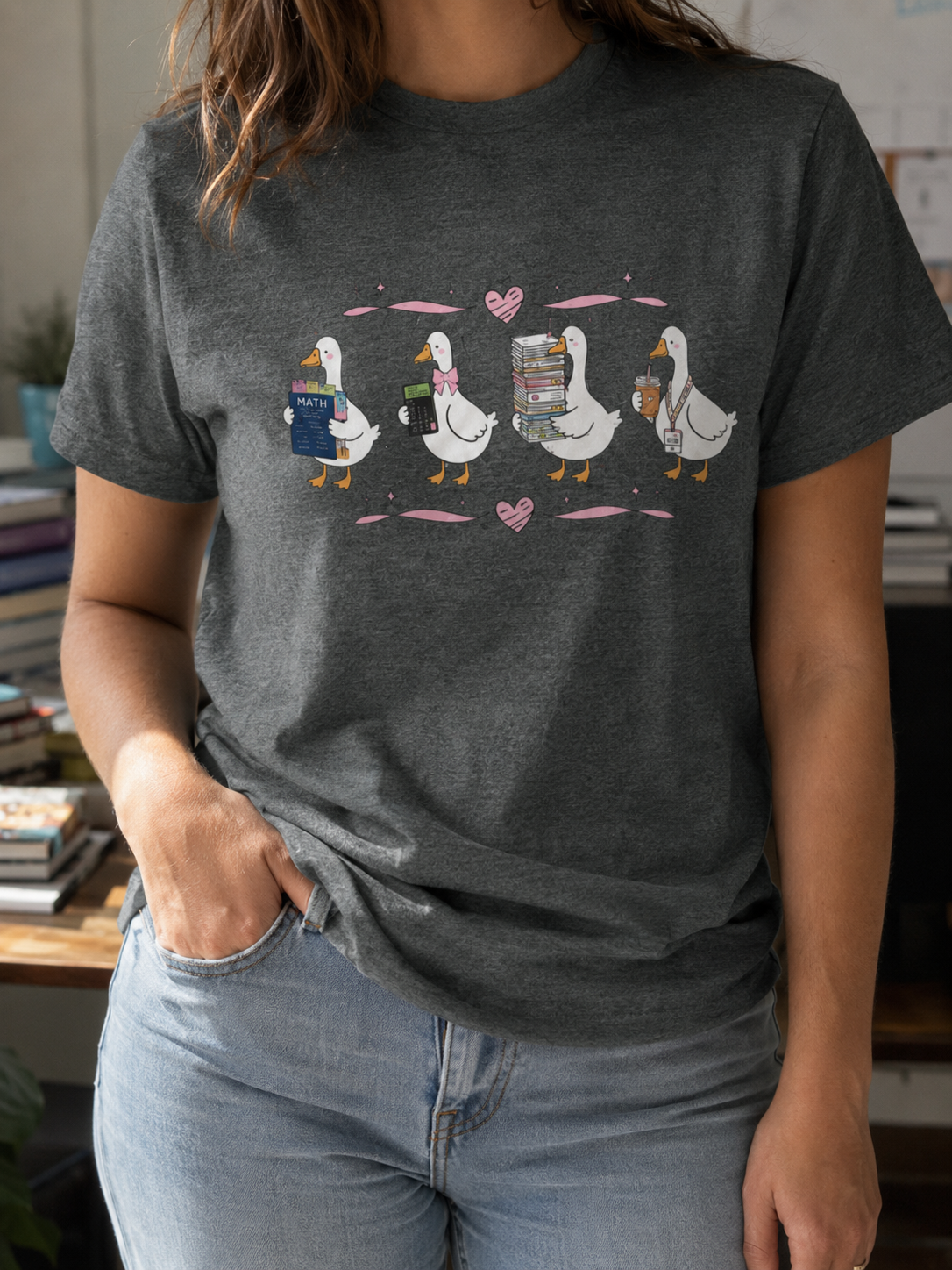 Bella + Canvas 3001 unisex t-shirt in Deep Heather featuring four adorable math teacher geese with a math textbook, calculator, stack of books, and iced coffee. A cute math teacher shirt perfect for algebra, geometry, elementary, middle, or high school math teachers, school staff, and back-to-school outfits.