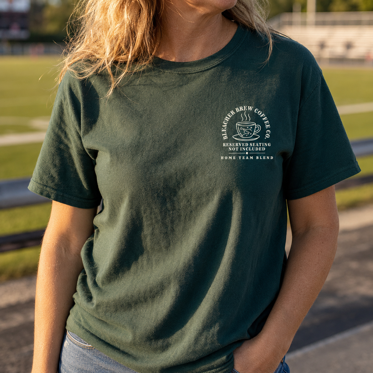 Bella + Canvas 3001 unisex t-shirt in Forest featuring a small left chest "Bleacher Brew Coffee Co." graphic with a coffee cup and the phrase "Reserved Seating Not Included. Home Team Blend." Comfortable sports mom graphic tee perfect for football games, soccer matches, baseball tournaments, weekend sidelines, and everyday casual wear.