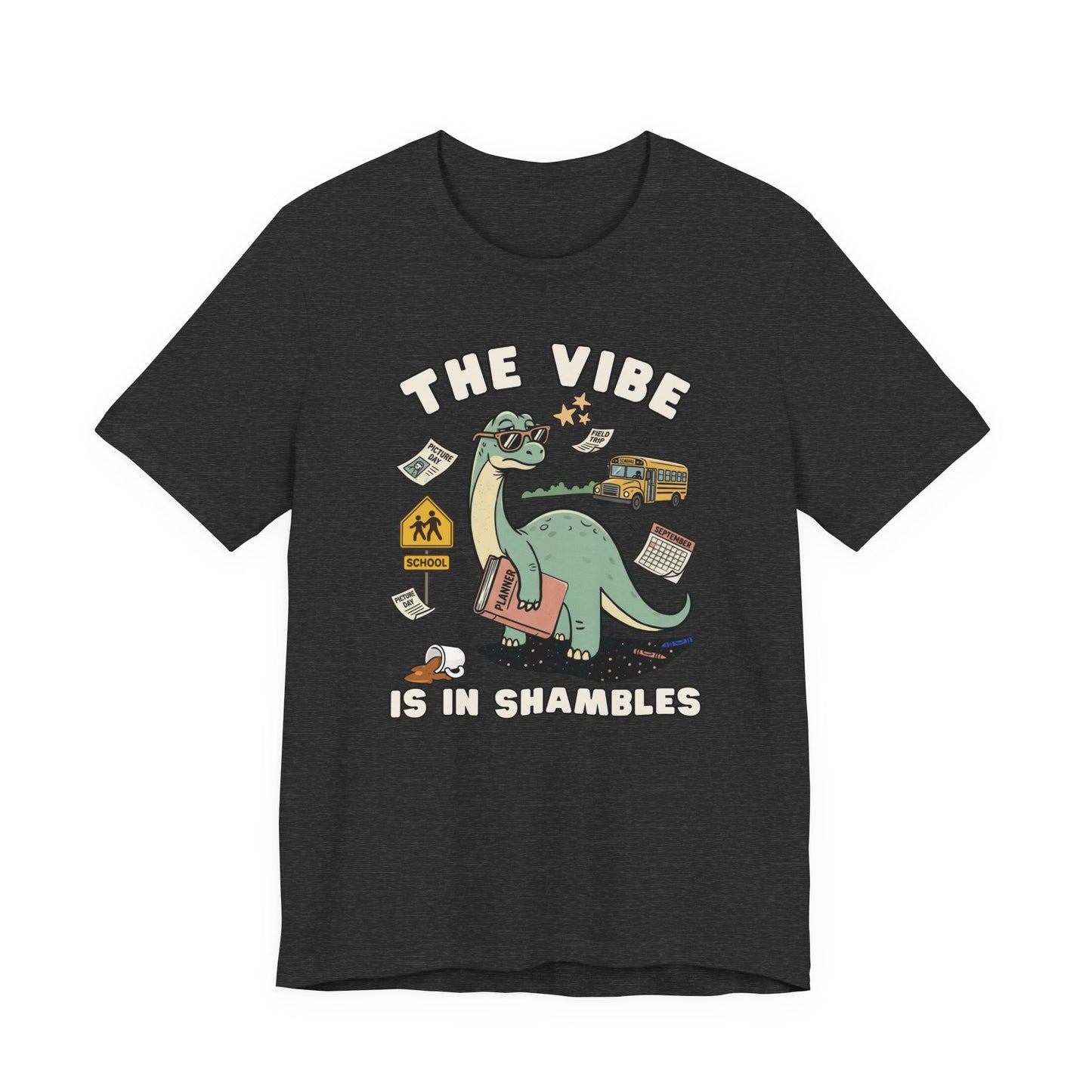 Bella + Canvas 3001 heather dark grey t-shirt featuring a humorous teacher dinosaur design with the phrase "The Vibe Is In Shambles." The graphic shows a dinosaur holding a planner and surrounded by a school bus, classroom supplies, a spilled coffee cup, a calendar, and back-to-school icons. Perfect for teachers, educators, school staff, elementary teachers, and anyone embracing the organized chaos of the school year with humor and style.