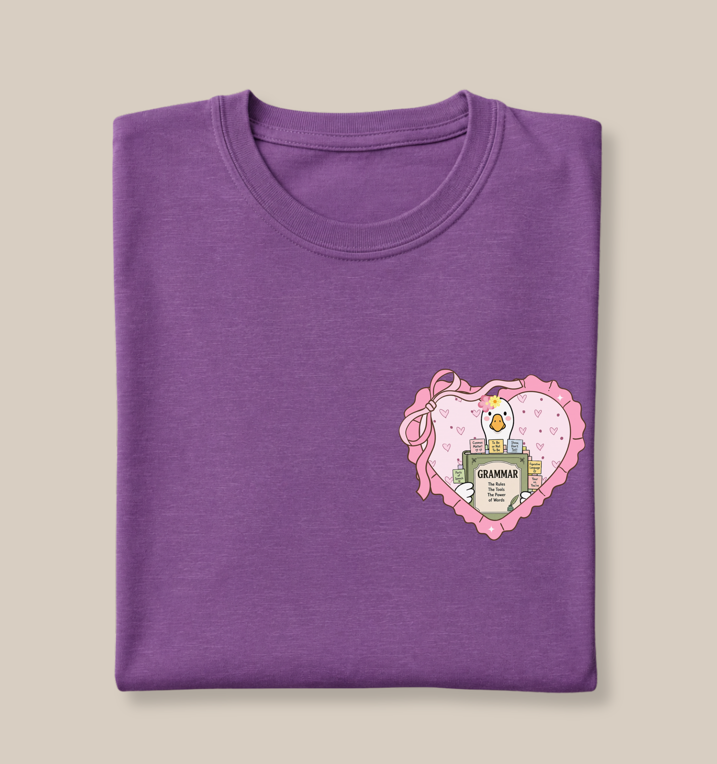 Bella + Canvas 3001 t-shirt in Heather Team Purple featuring a coquette English teacher goose heart pocket design. The artwork shows a white goose holding a grammar book inside a pink heart with ribbon accents and colorful grammar note tabs. Perfect for English teachers, language arts educators, reading teachers, and back-to-school teacher gifts.