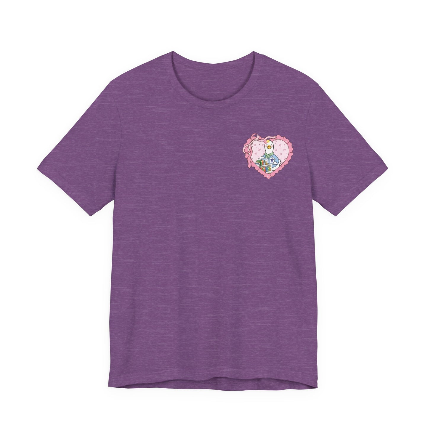 Bella + Canvas 3001 t-shirt in Heather Team Purple featuring a coquette school librarian goose pocket design. The artwork shows a white goose behind a colorful library cart inside a pink heart with ribbon accents. Great for librarians, library aides, and reading advocates.