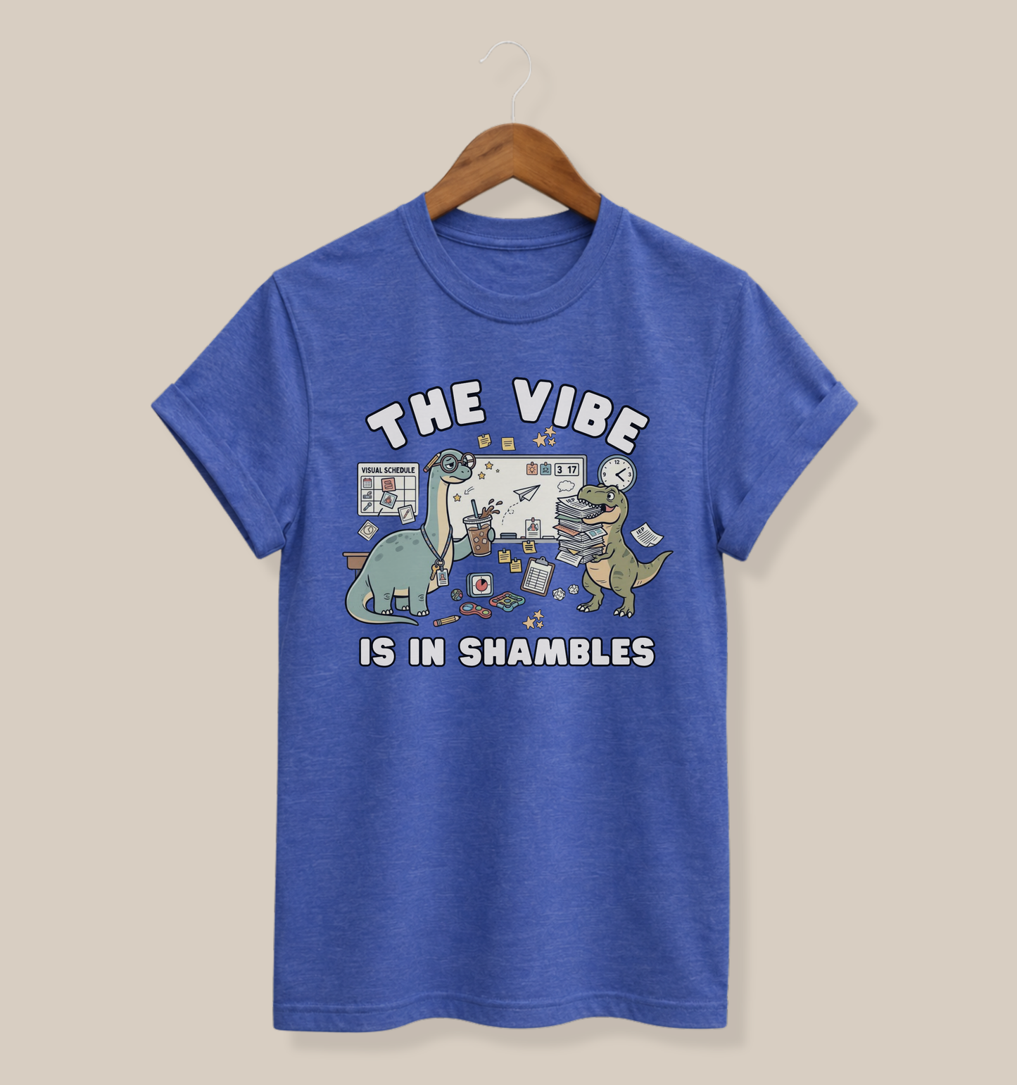 Bella + Canvas 3001 heather true royal blue t-shirt featuring a funny special education teacher dinosaur design with the phrase "The Vibe Is In Shambles." The graphic includes dinosaurs surrounded by visual schedules, paperwork, fidget toys, classroom supplies, a clock, and school organization tools. Perfect for special education teachers, IEP teachers, paraprofessionals, school staff, and educators who understand classroom chaos with humor.