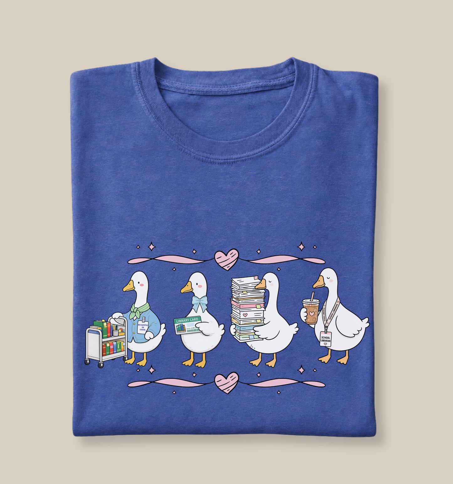 Bella + Canvas 3001 t-shirt in Heather True Royal featuring a coquette librarian goose design. Four white geese display a book cart, library card, stack of books, and iced coffee with a school librarian badge. Pink hearts and ribbon accents create a whimsical look, making this cute librarian shirt perfect for school librarians, library staff, book lovers, teacher appreciation gifts, and back-to-school outfits.
