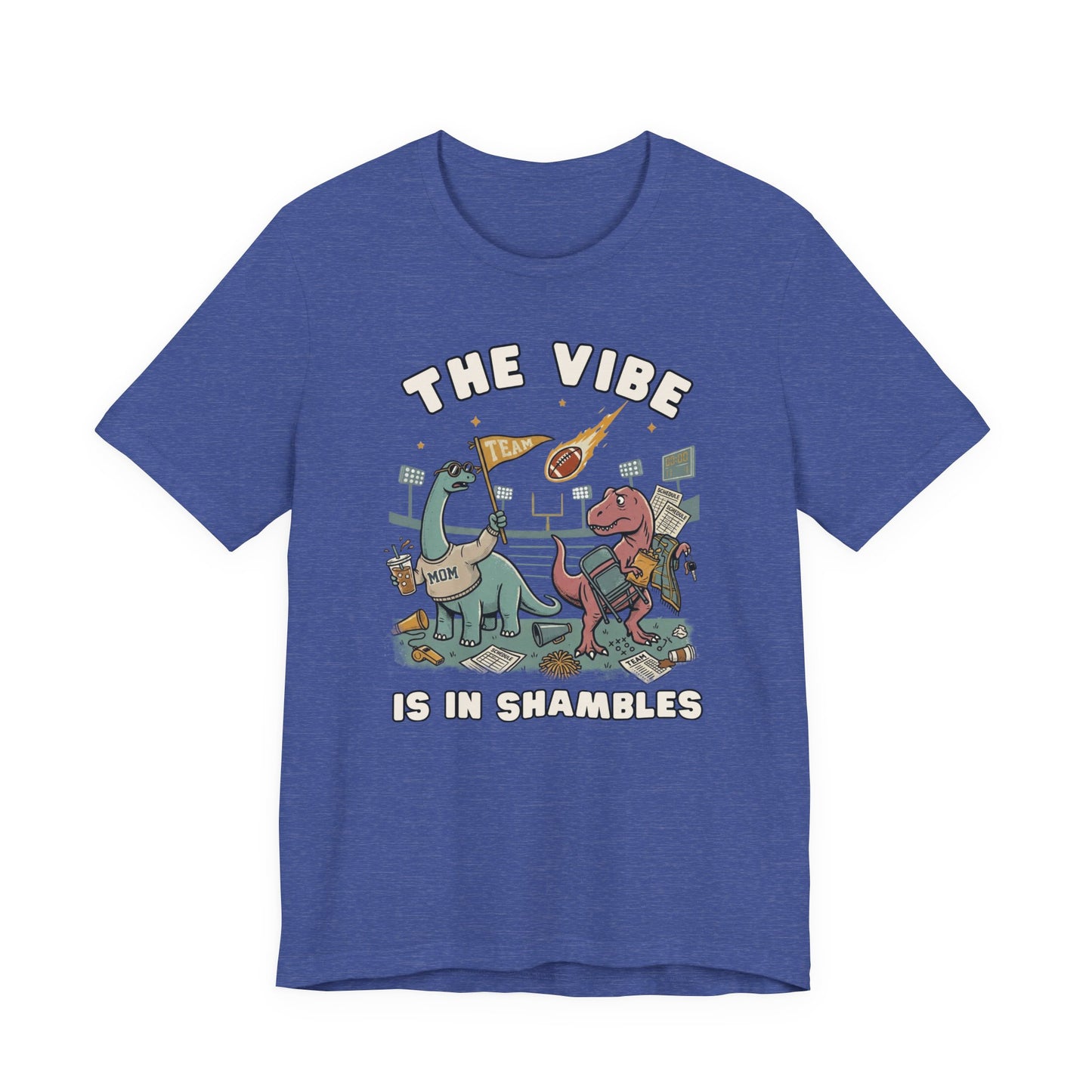 Bella + Canvas 3001 heather true royal blue t-shirt featuring two overwhelmed dinosaurs at a football stadium surrounded by a folding chair, coffee, snacks, schedule papers, and team gear. Funny sports mom graphic tee with "The Vibe Is In Shambles" design, perfect for football moms, sports parents, game day outfits, tailgates, and sports season gifts.