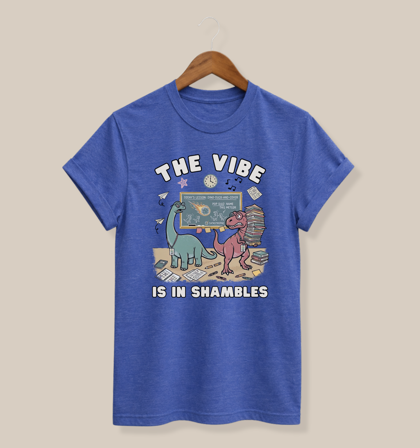 Bella + Canvas 3001 heather true royal blue t-shirt featuring two overwhelmed dinosaurs in a chaotic classroom with books, papers, crayons, and a chalkboard. Funny teacher shirt with "The Vibe Is In Shambles" design, perfect for teachers, educators, classroom humor, back-to-school outfits, and teacher appreciation gifts.
