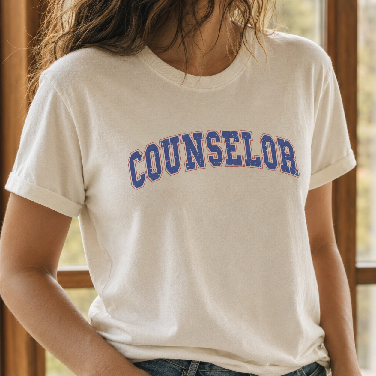 Bella + Canvas 3001 unisex t-shirt in Natural featuring a distressed varsity-style "Counselor" graphic in blue with a pink outline across the chest. A retro-inspired graphic tee for school counselors, guidance counselors, and education professionals, perfect for school days, casual wear, and counselor appreciation gifts.