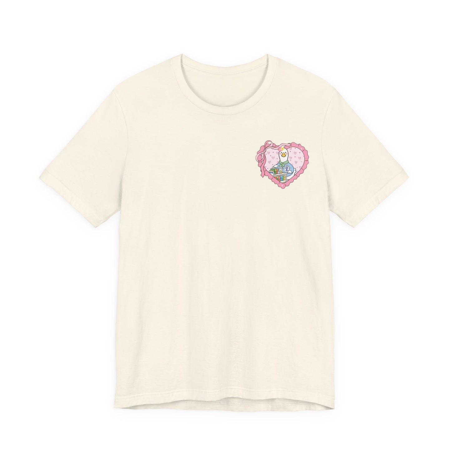Bella + Canvas 3001 t-shirt in Natural featuring a coquette school librarian goose pocket design. The artwork shows a white goose behind a colorful library cart inside a pink heart with ribbon details. Ideal for librarians, teachers, and avid readers.