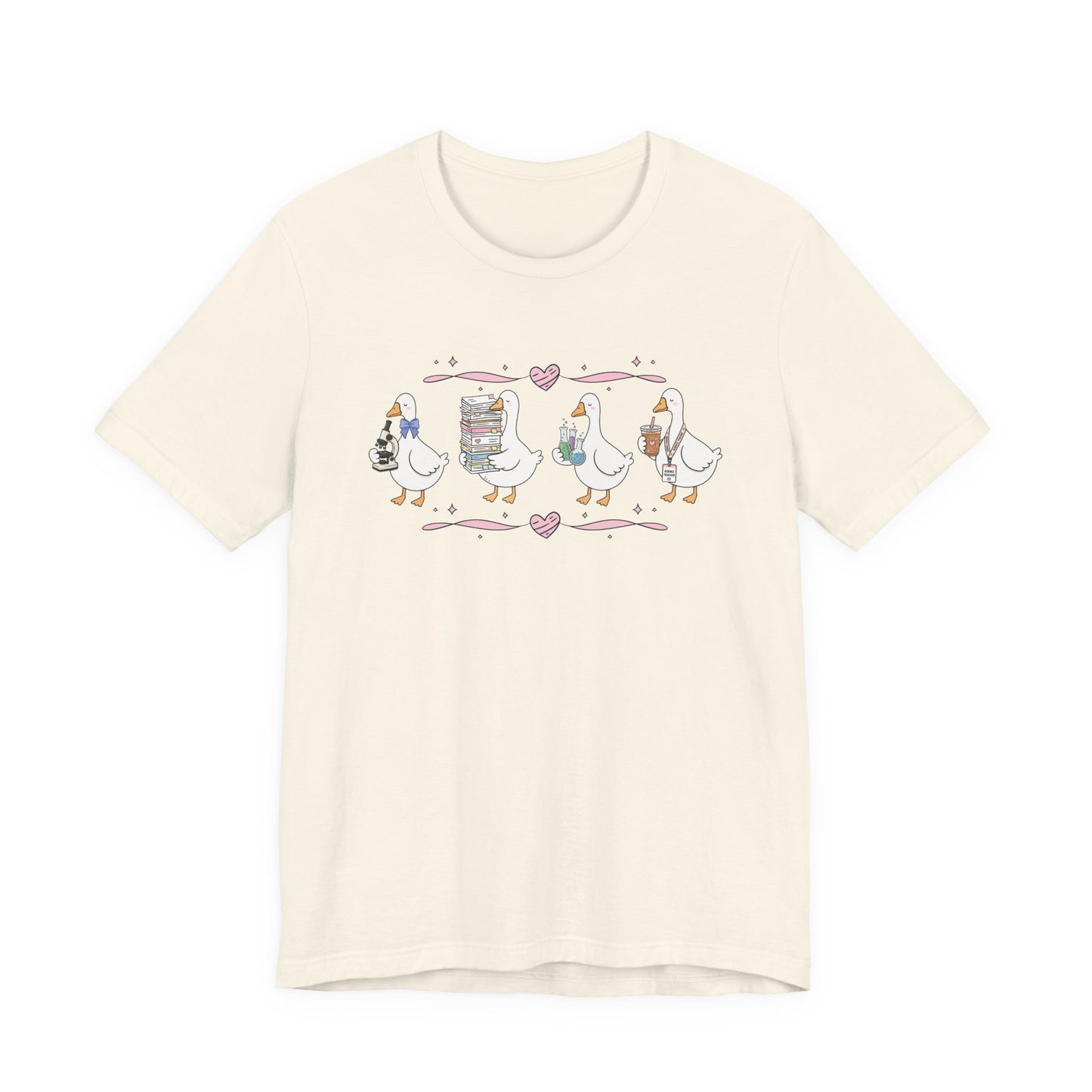 Bella + Canvas 3001 t-shirt in Natural featuring a coquette science teacher goose design. Four white geese hold a microscope, a stack of classroom papers, science beakers filled with colorful experiments, and an iced coffee with a science teacher lanyard. Pink hearts and ribbon accents add a charming touch, making this science teacher shirt a thoughtful gift for science educators, teacher appreciation events, and back-to-school season.