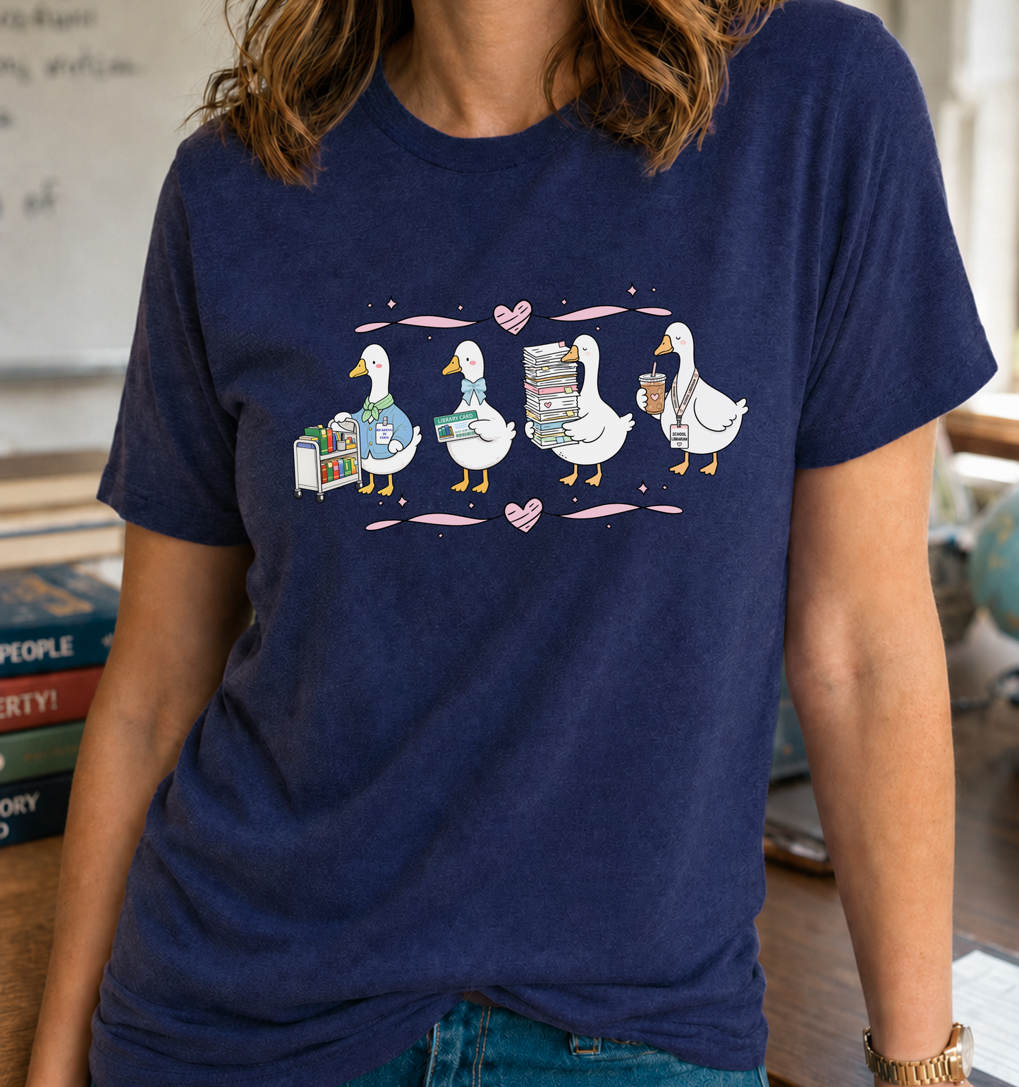 Bella + Canvas 3001 unisex t-shirt in Navy featuring four adorable librarian geese with a library cart, library card, stack of books, and coffee. A cute school librarian shirt perfect for librarians, media specialists, library staff, book lovers, and back-to-school outfits.