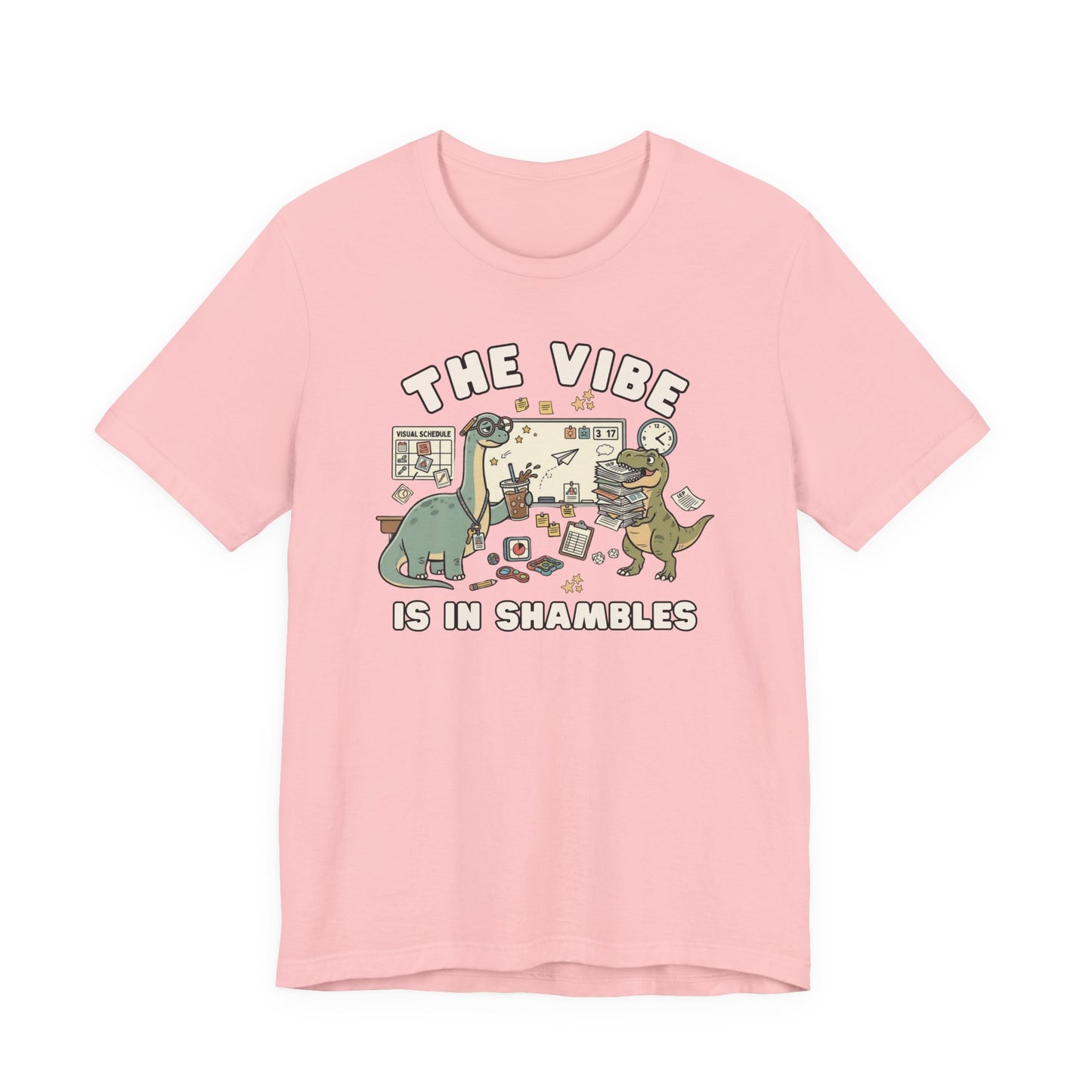 Bella + Canvas 3001 pink t-shirt featuring a funny special education teacher dinosaur design with the phrase "The Vibe Is In Shambles." The graphic includes dinosaurs surrounded by visual schedules, classroom supplies, paperwork, fidget toys, a clock, and teaching materials. Perfect for special education teachers, IEP teachers, paraprofessionals, school staff, and educators who appreciate humorous classroom-themed apparel.