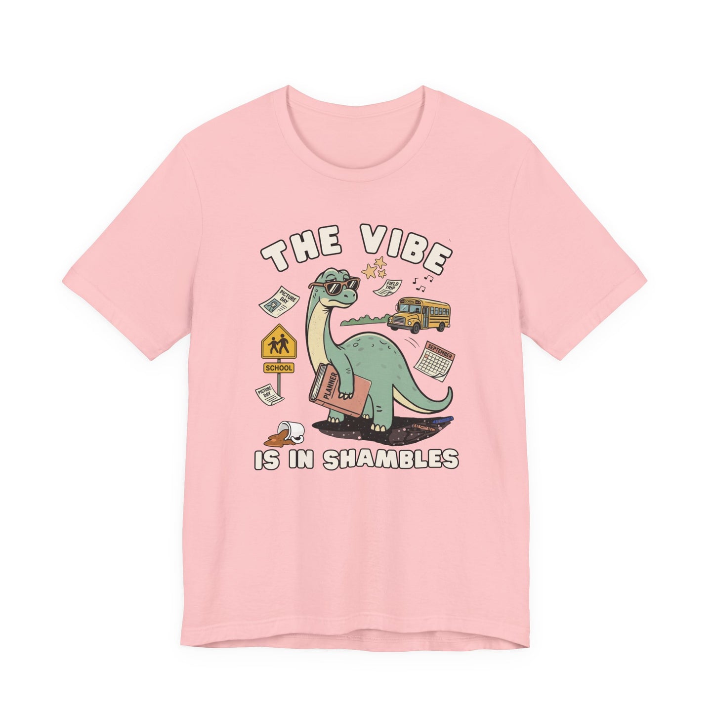 Bella + Canvas 3001 pink t-shirt featuring a funny teacher dinosaur design with the phrase "The Vibe Is In Shambles." The graphic shows a dinosaur holding a planner and surrounded by a school bus, classroom supplies, a spilled coffee cup, a calendar, and back-to-school icons. Perfect for teachers, educators, school staff, elementary teachers, and anyone embracing the chaos of the school year with humor and style.