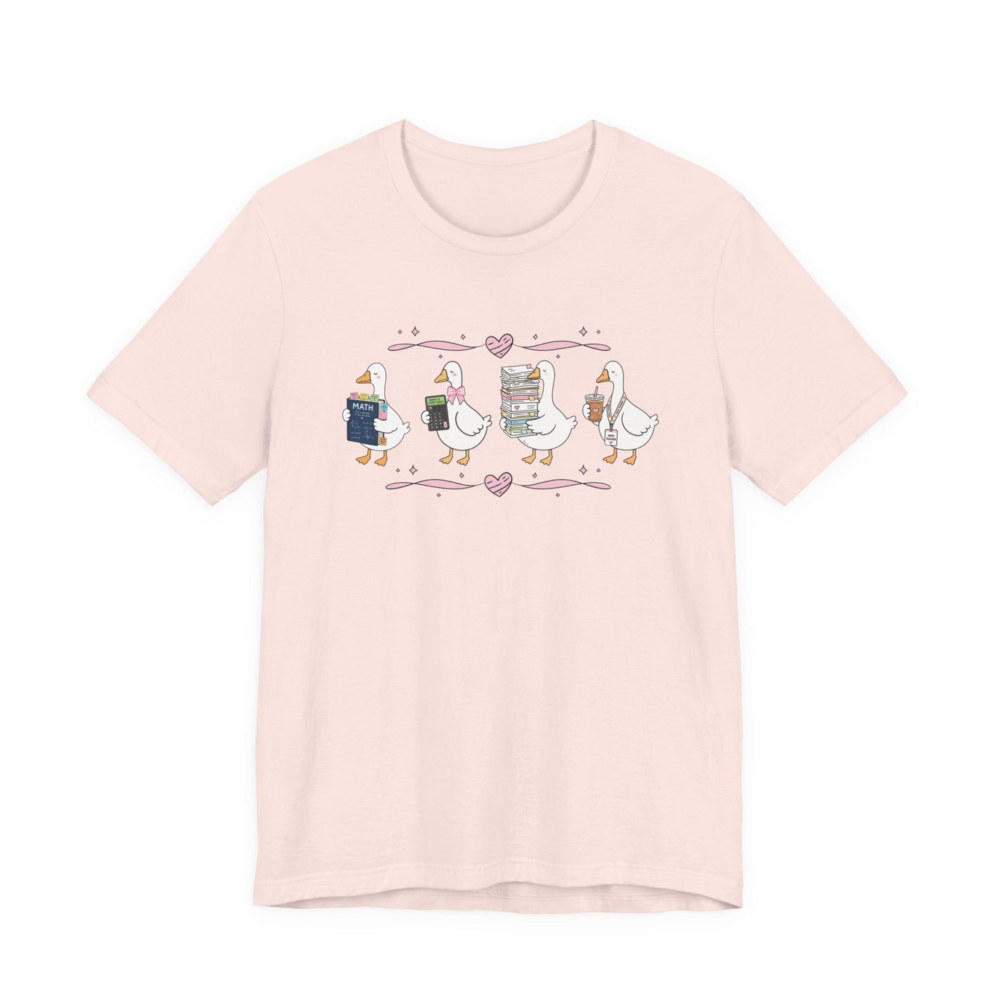 Bella + Canvas 3001 t-shirt in Soft Pink featuring a coquette math teacher goose design. Four white geese carry a math textbook, calculator, stack of papers, and iced coffee with a teacher lanyard. Pink bows and heart accents add a whimsical touch. This cute math teacher shirt is perfect for back-to-school outfits, teacher appreciation gifts, and everyday classroom wear.
