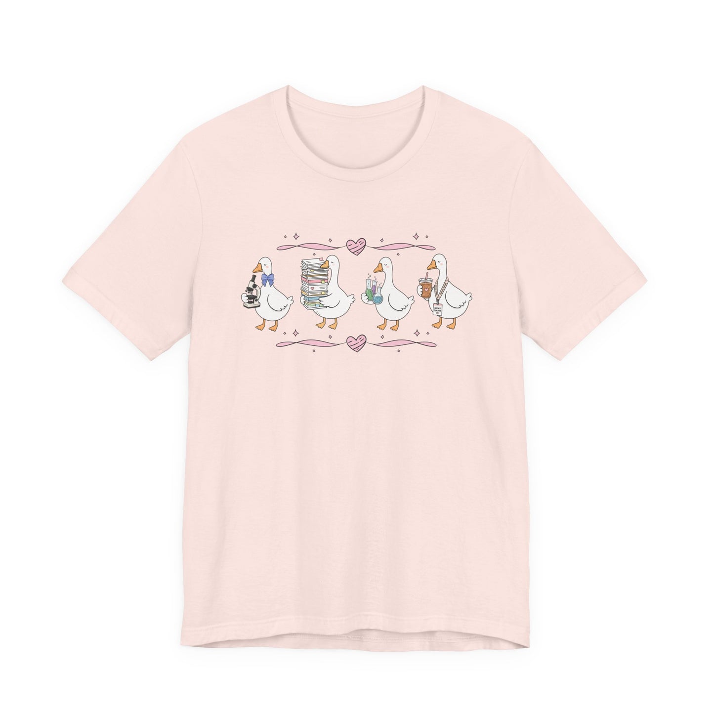 Bella + Canvas 3001 t-shirt in Soft Pink featuring a coquette science teacher goose design. Four white geese hold a microscope, a stack of classroom papers, science beakers filled with colorful experiments, and an iced coffee with a science teacher lanyard. Pink hearts and ribbon accents create a sweet, whimsical look, making this cute science teacher shirt perfect for back-to-school outfits, teacher appreciation gifts, and everyday classroom wear.