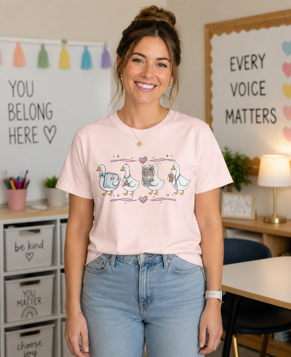 Female teacher wearing a Bella + Canvas 3001 t-shirt in Soft Pink featuring a coquette special education teacher goose design. Four white geese hold an IEP binder, sensory fidget toy, stack of paperwork, and iced coffee with a special education teacher lanyard. Pink hearts and ribbon accents add a playful touch. Styled in a special education classroom, this cute SPED teacher shirt is perfect for back-to-school outfits, teacher appreciation gifts, and everyday classroom wear.