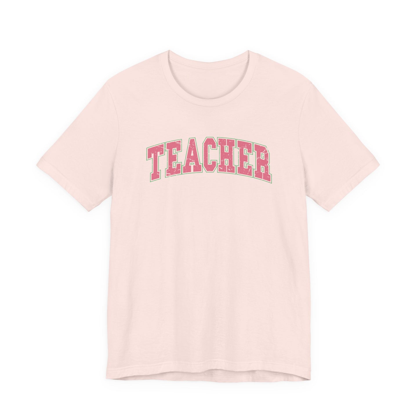 Bella + Canvas 3001 unisex t-shirt in Soft Pink featuring a distressed varsity-style "Teacher" graphic in pink with a green outline. A trendy teacher tee with a collegiate-inspired design, perfect for teachers, school staff, classroom wear, and back-to-school season.
