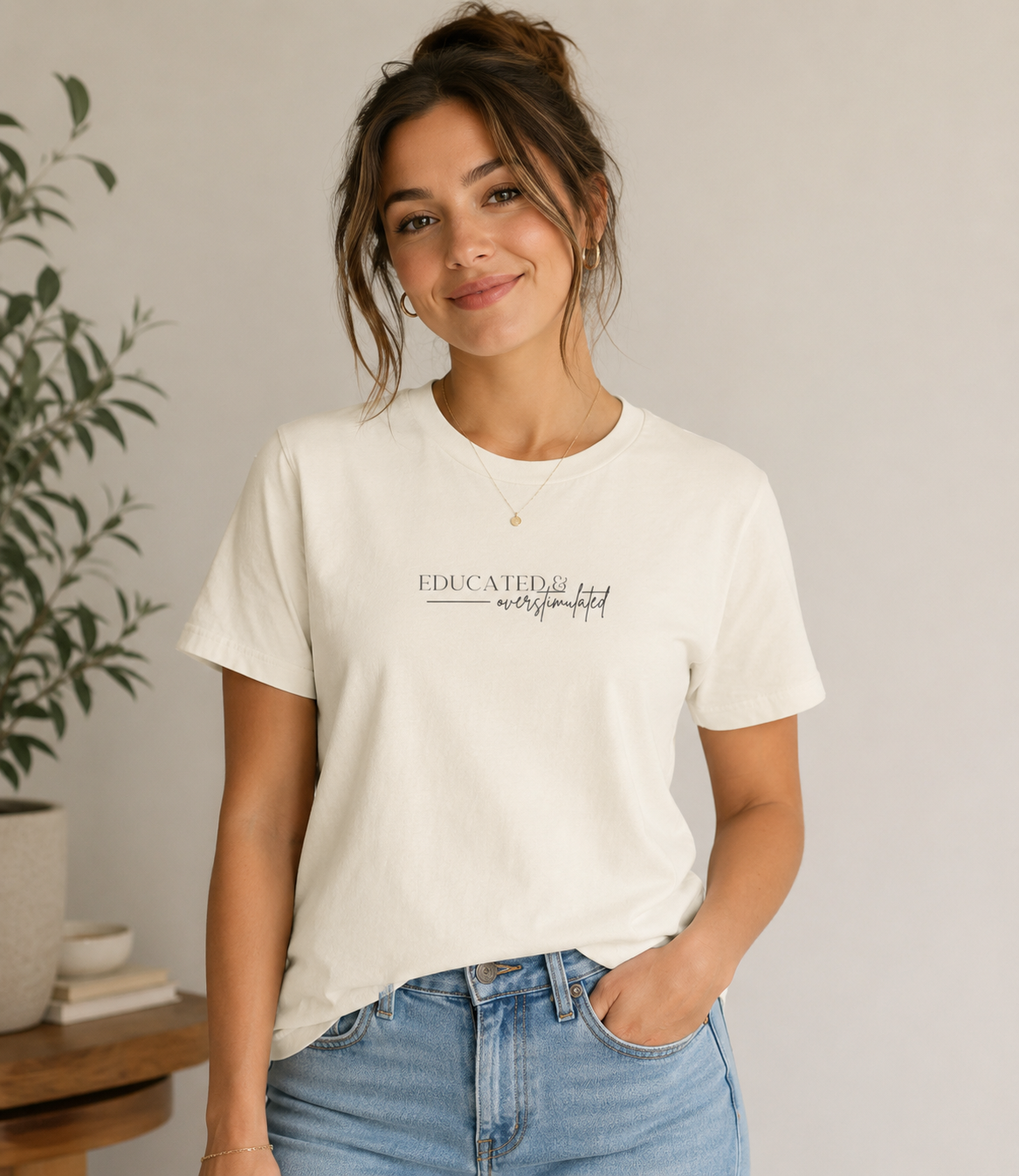 Woman wearing a Bella + Canvas 3001 t-shirt in natural featuring a minimalist “Educated & overstimulated” graphic with neutral typography and a simple aesthetic design.