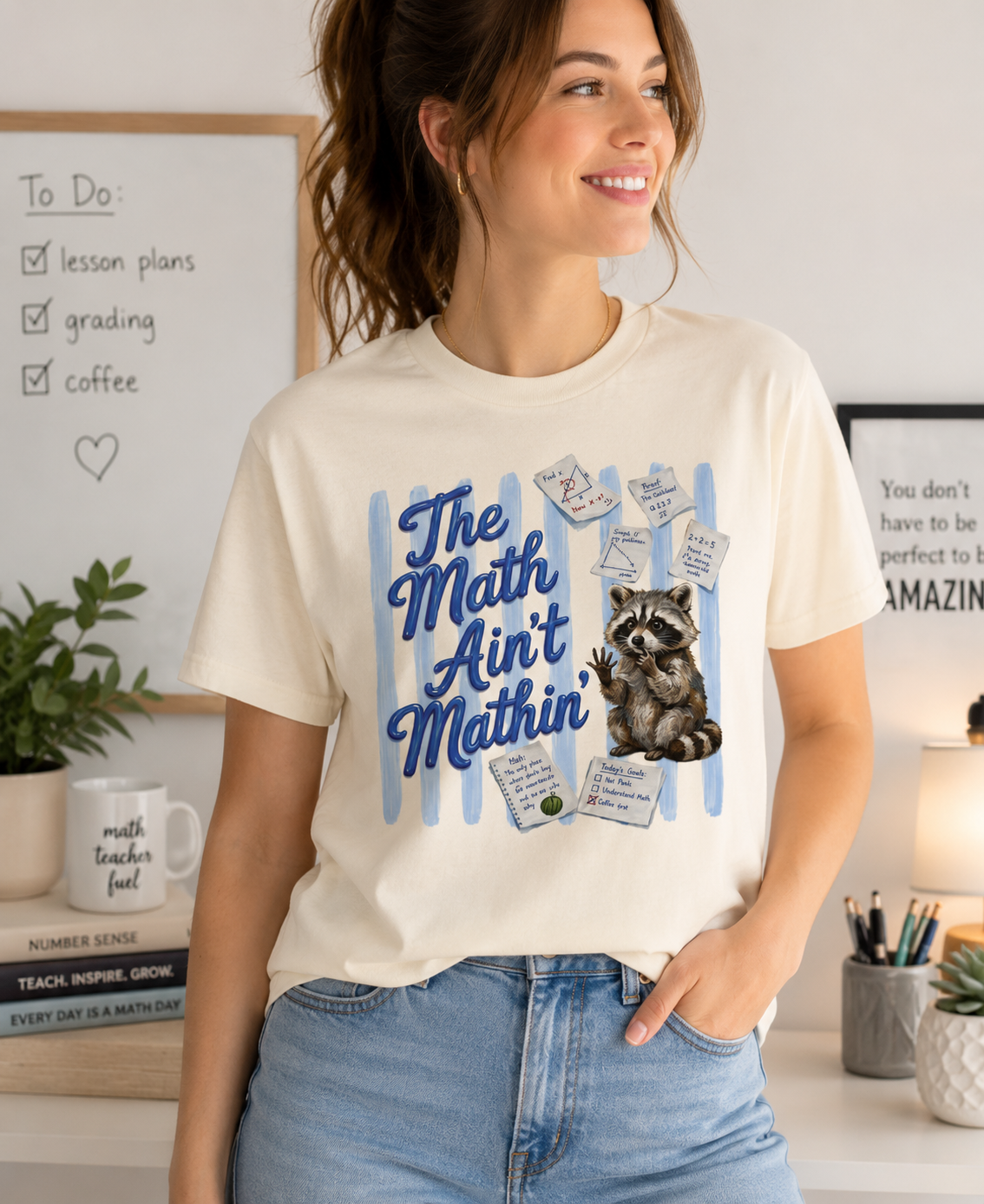 Bella + Canvas 3001 t-shirt in natural featuring the phrase “The Math Ain’t Mathin’” in blue script with a puzzled raccoon surrounded by math equations, geometry notes, classroom reminders, and problem-solving worksheets. Funny math teacher shirt for algebra teachers, geometry teachers, middle school educators, high school math teachers, tutors, and STEM professionals who enjoy classroom humor.