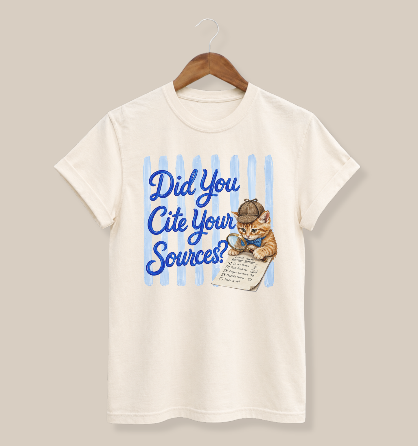 Bella + Canvas 3001 t-shirt in natural featuring the phrase “Did You Cite Your Sources?” in blue script with a detective kitten using a magnifying glass to review a paper. Funny English teacher shirt for educators, librarians, reading specialists, and literature lovers.