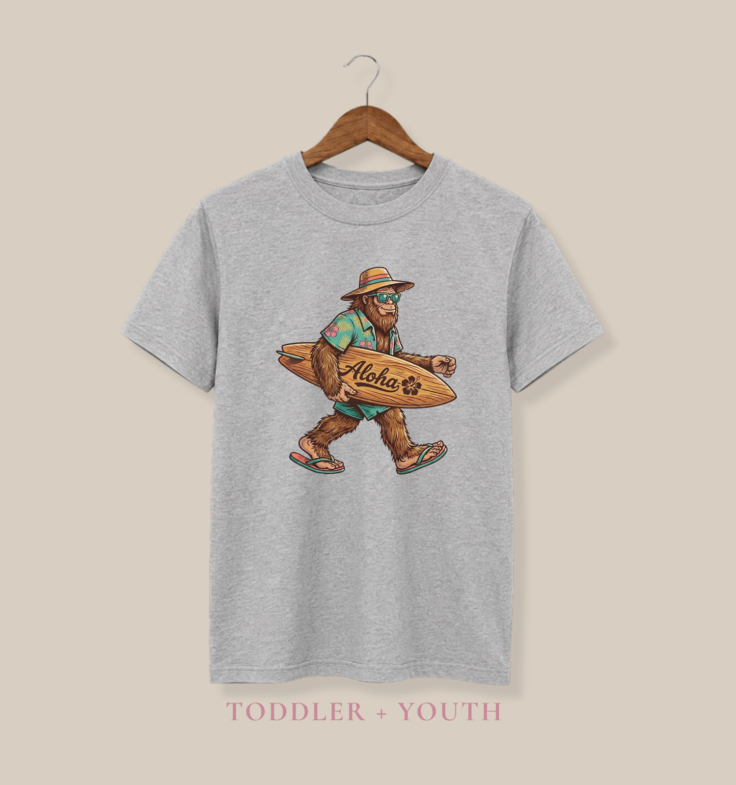 Bella + Canvas 3001Y youth t-shirt in athletic heather grey featuring a Bigfoot wearing a tropical shirt and sunglasses while carrying an “Aloha” surfboard and walking in flip flops.

