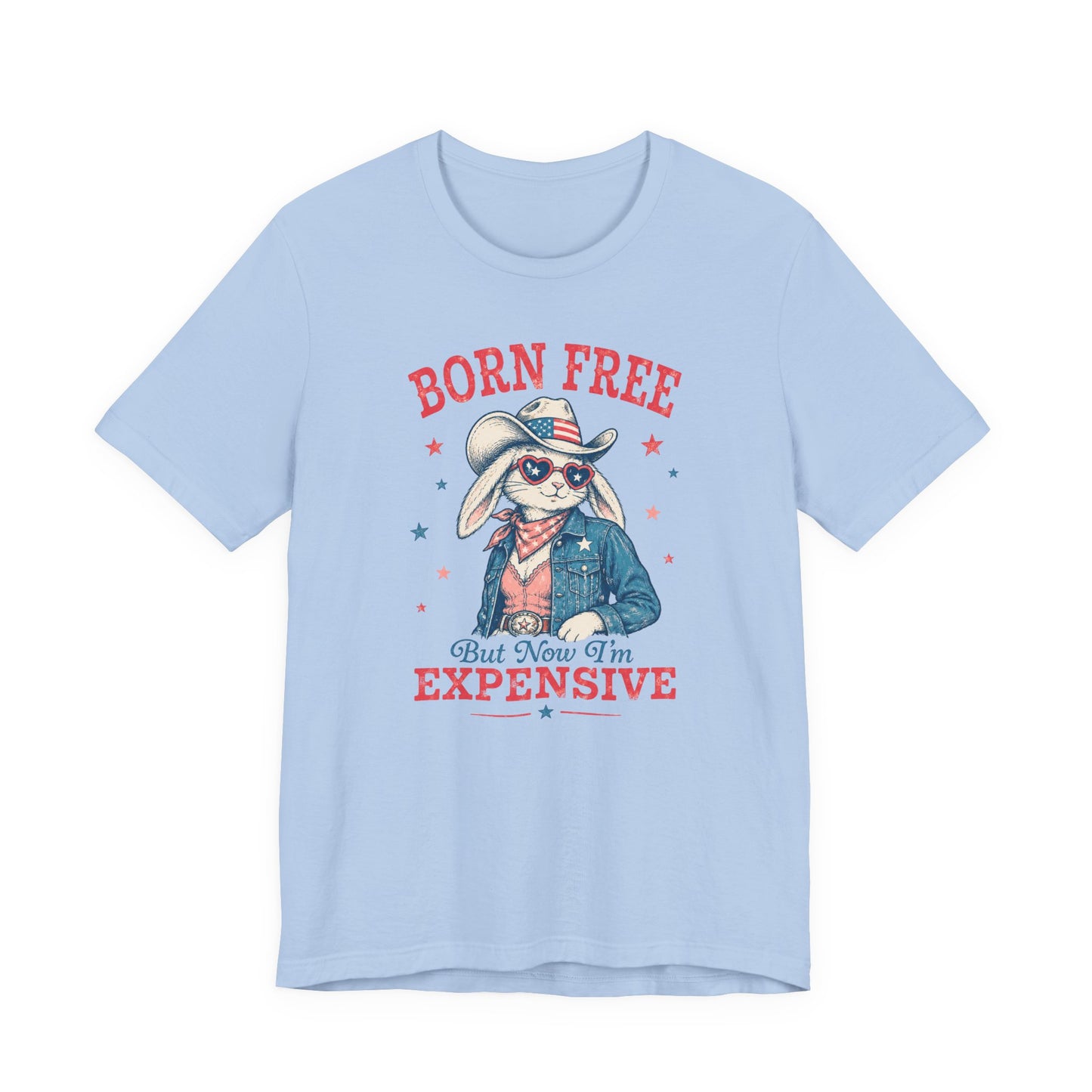Adult Bella + Canvas baby blue t-shirt featuring a patriotic bunny cowgirl graphic with heart-shaped sunglasses, an American flag cowboy hat, denim jacket, and the phrase “Born Free But Now I’m Expensive” in distressed red and blue lettering.