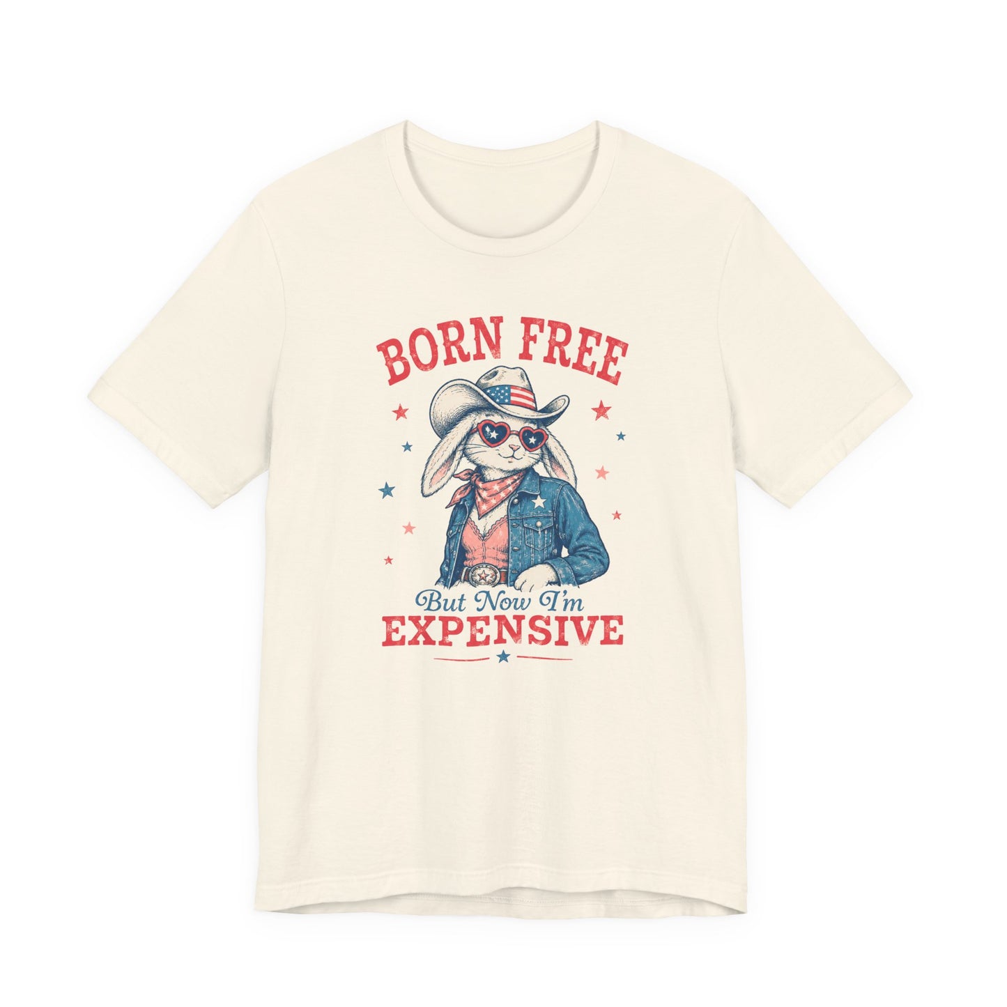 Adult Bella + Canvas natural colored t-shirt featuring a patriotic bunny cowgirl graphic with heart sunglasses, American flag cowboy hat, denim jacket, and the phrase “Born Free But Now I’m Expensive” in vintage distressed red and blue lettering.