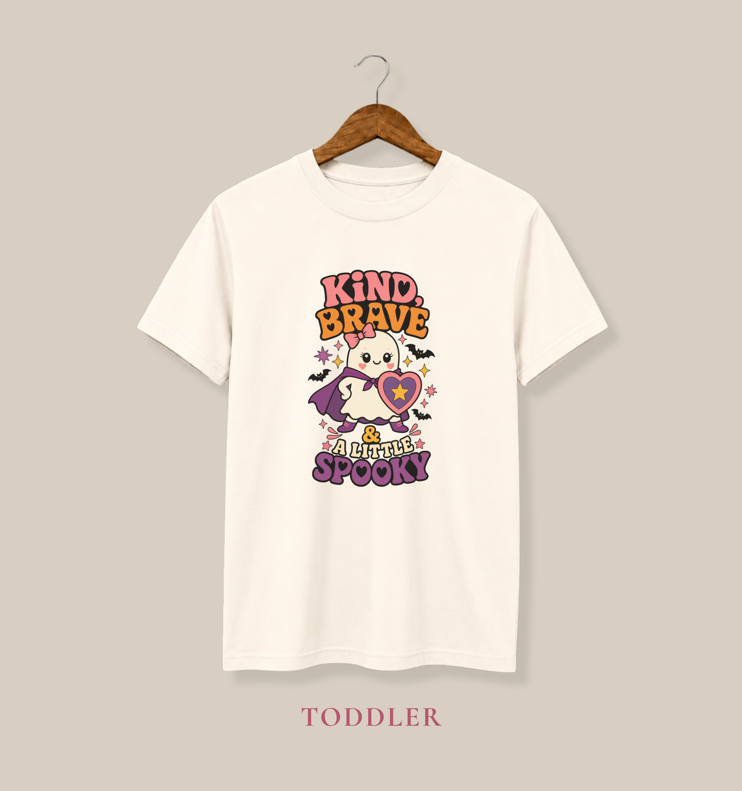 Natural toddler T-shirt featuring a caped ghost with a heart shield and the phrase “Kind, Brave & a Little Spooky.”