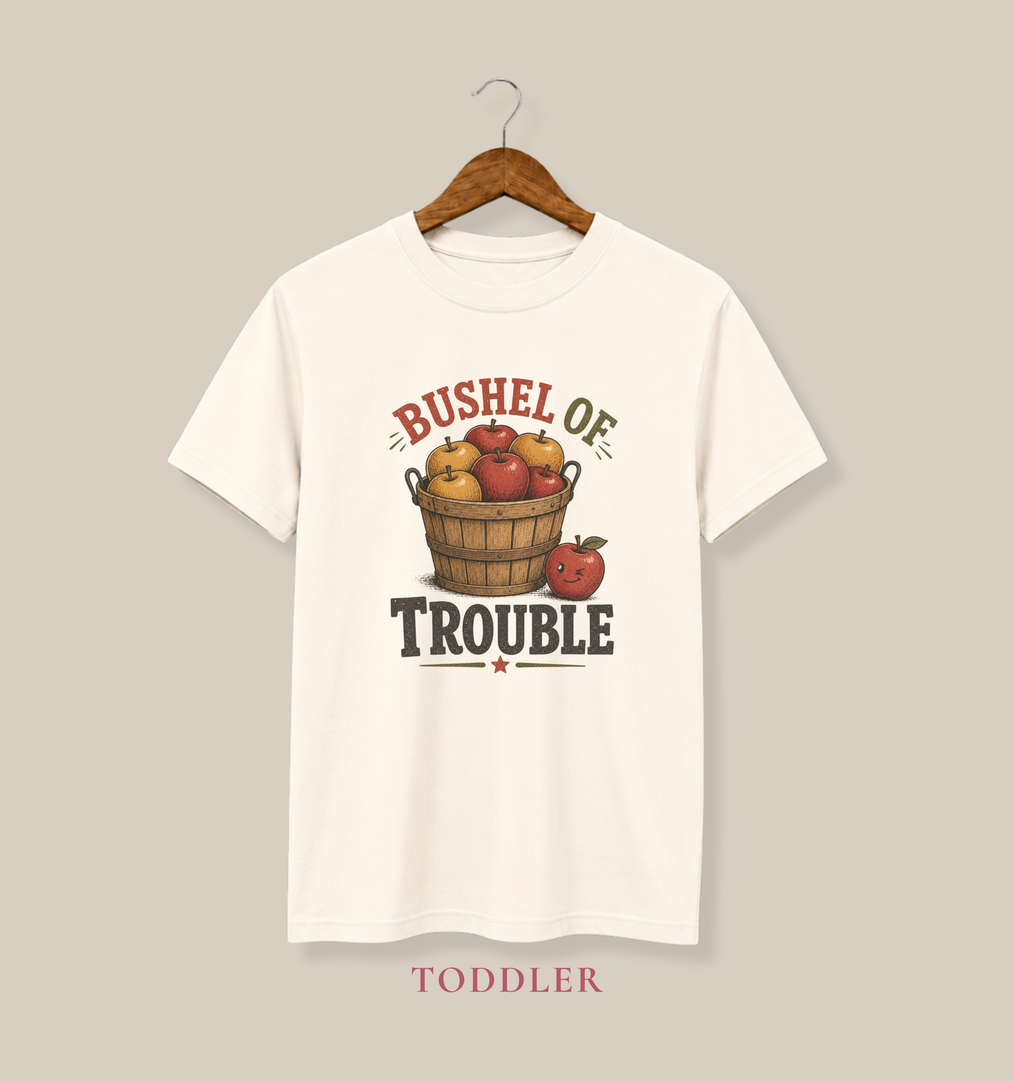 Natural  Color toddler T-shirt featuring a vintage apple basket graphic and the phrase “Bushel of Trouble.”