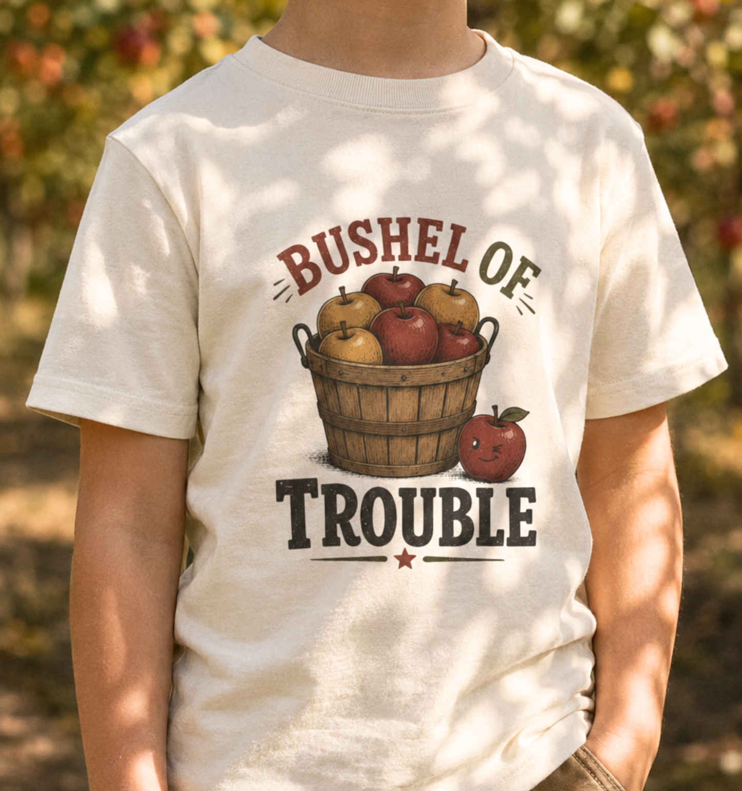 Child wearing a natural toddler T-shirt featuring a vintage apple basket design with the phrase “Bushel of Trouble.”
