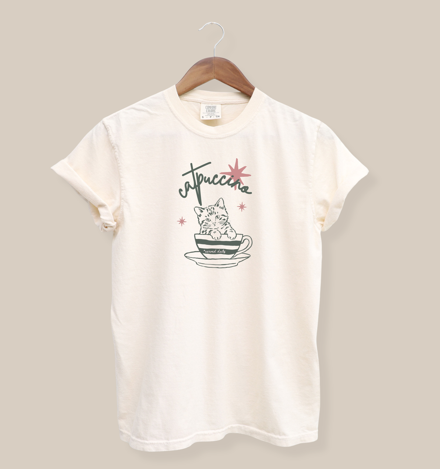 Ivory Comfort Colors 1717 t-shirt featuring a minimalist cat-in-a-coffee-cup graphic with retro stars and the word “Catuccine” in playful script lettering.