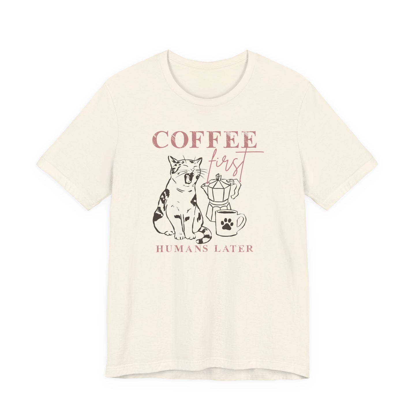 Bella + Canvas 3001 unisex t-shirt in ivory featuring a “Coffee First Humans Later” graphic with a sleepy cat, moka pot, and coffee mug illustration.