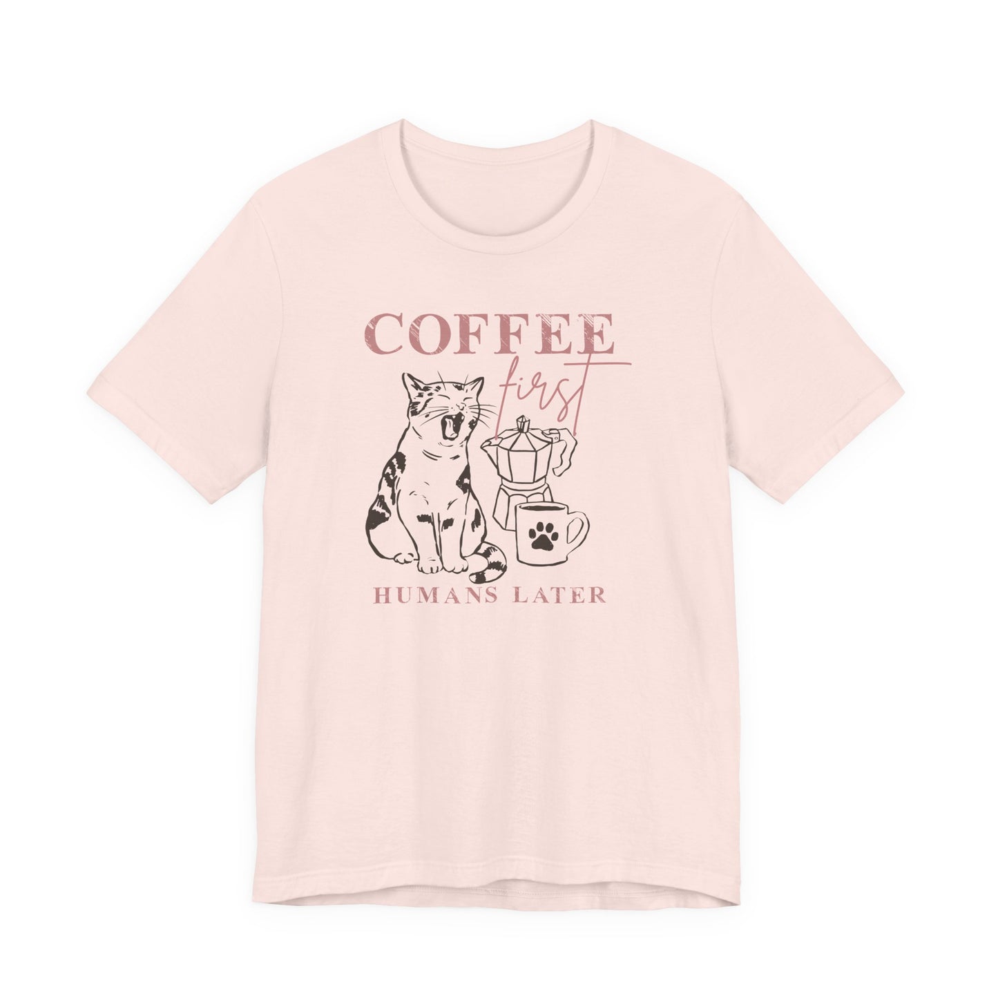 Bella + Canvas 3001 unisex t-shirt in soft pink featuring a “Coffee First Humans Later” graphic with a sleepy cat, moka pot, and coffee mug illustration.