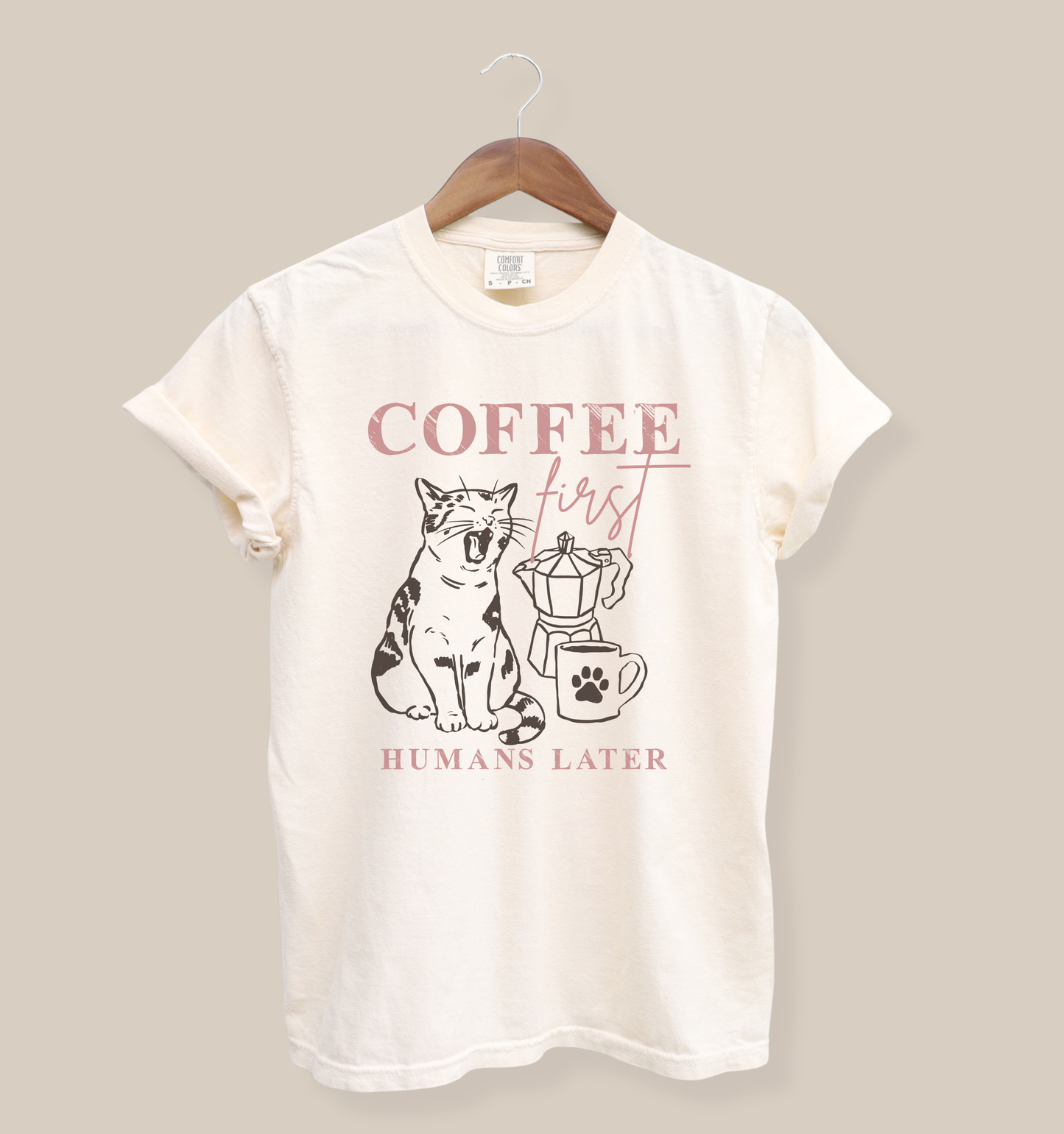 Ivory Comfort Colors 1717 t-shirt featuring a “Coffee First Humans Later” graphic with a sleepy cat, moka pot, and coffee mug design for cat lovers and coffee enthusiasts.