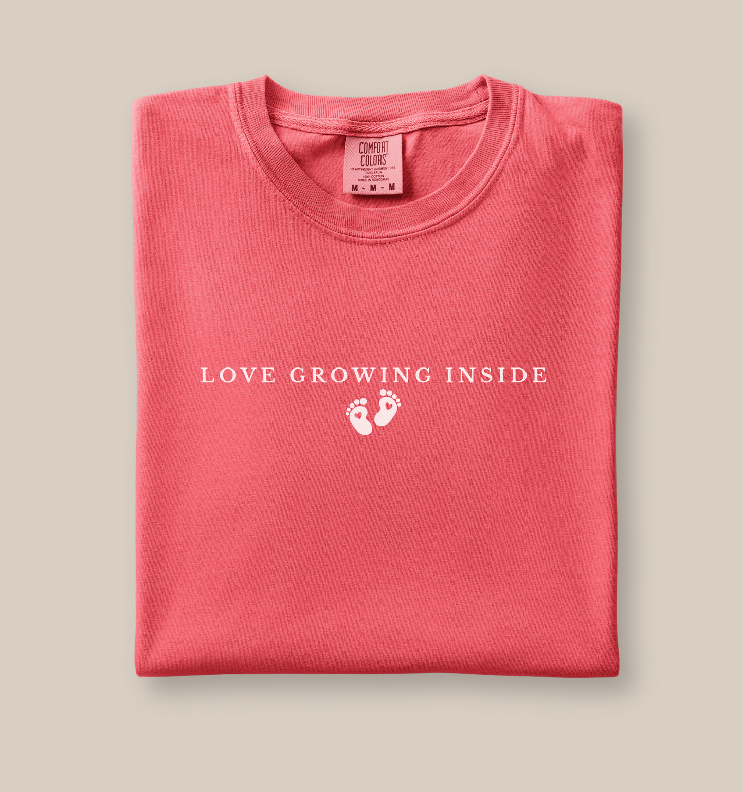 Folded t-shirt with 'Love Growing Inside' text and footprints on a beige background